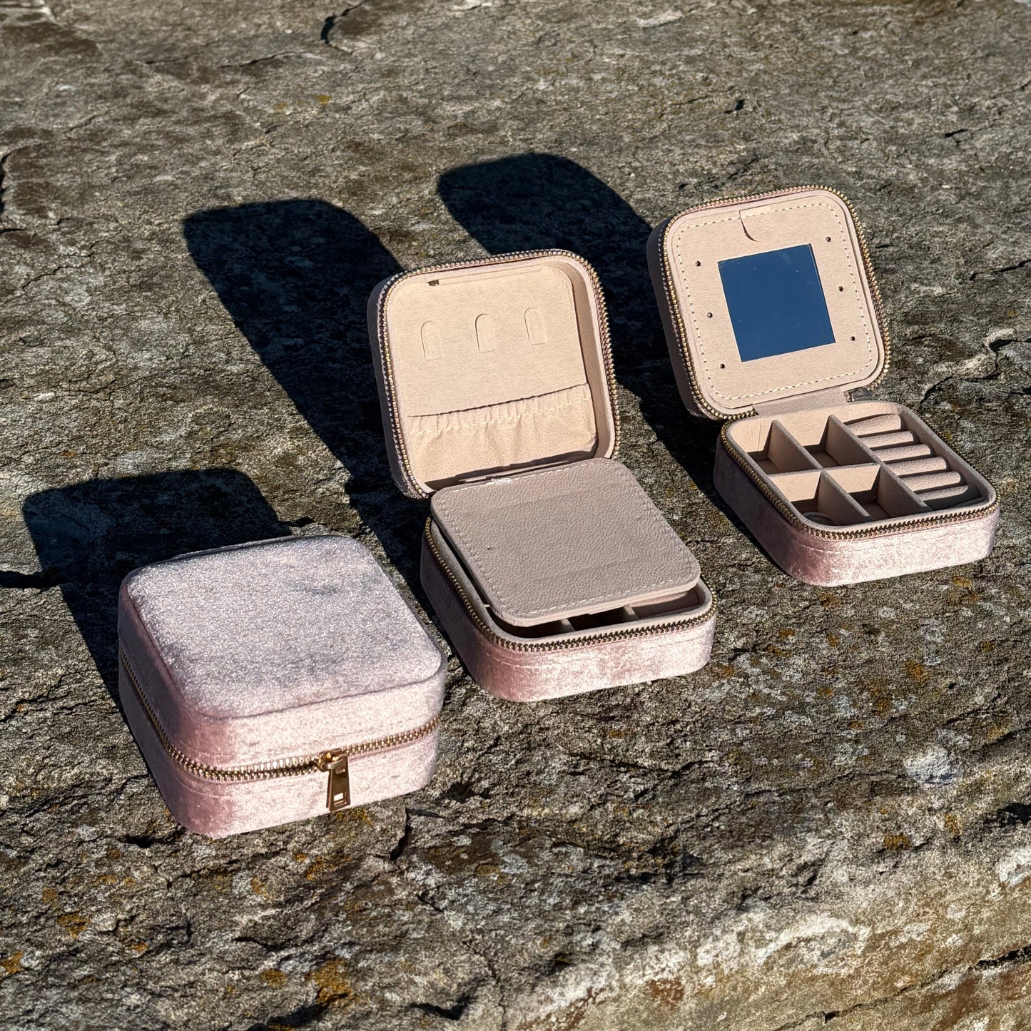 Three soft pink jewelry boxes on a textured stone surface