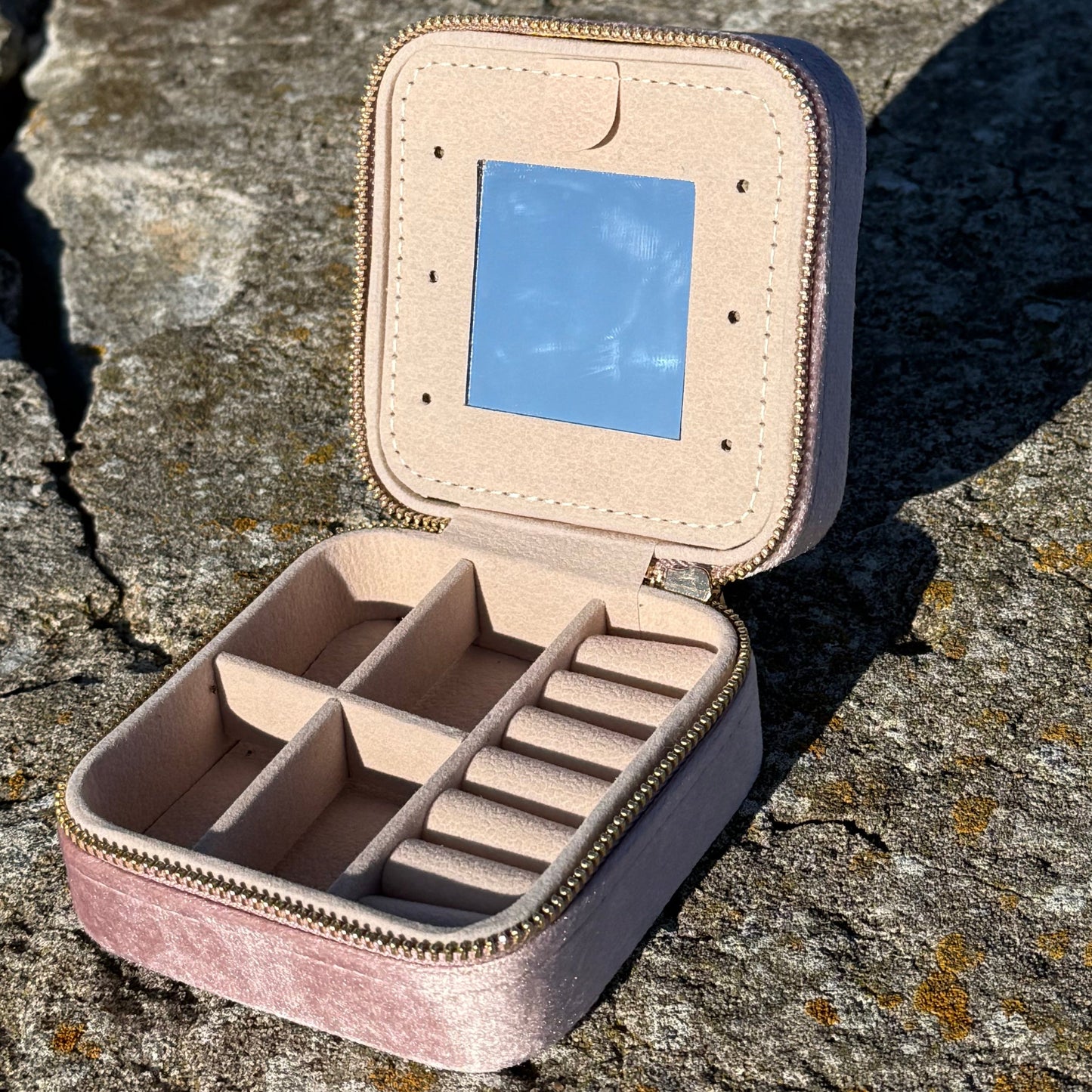 square jewelry box with mirror, pockets and folds for jewelry on a textured stone surface