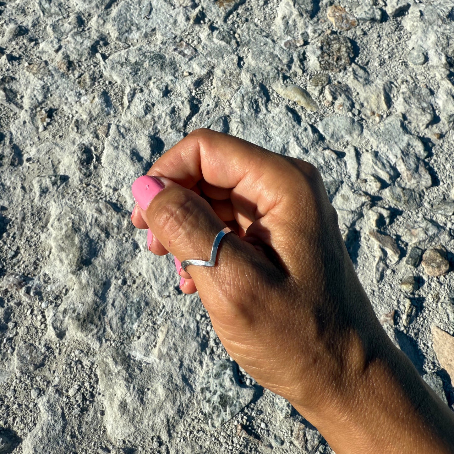 Hand with pink nail polish and a thumb silver ring on a textured gray surface