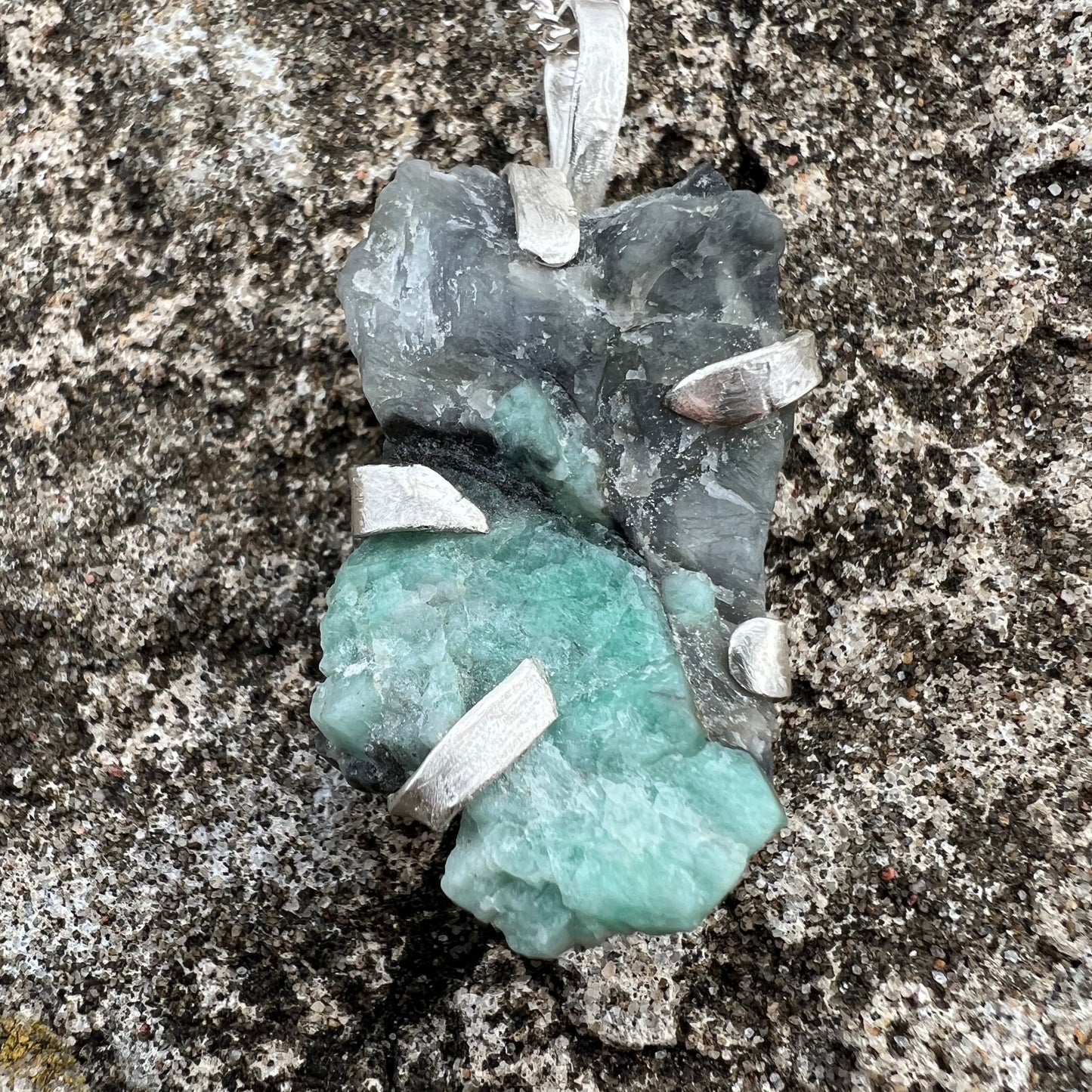 Necklace with a raw emerald pendant in silver on a textured surface