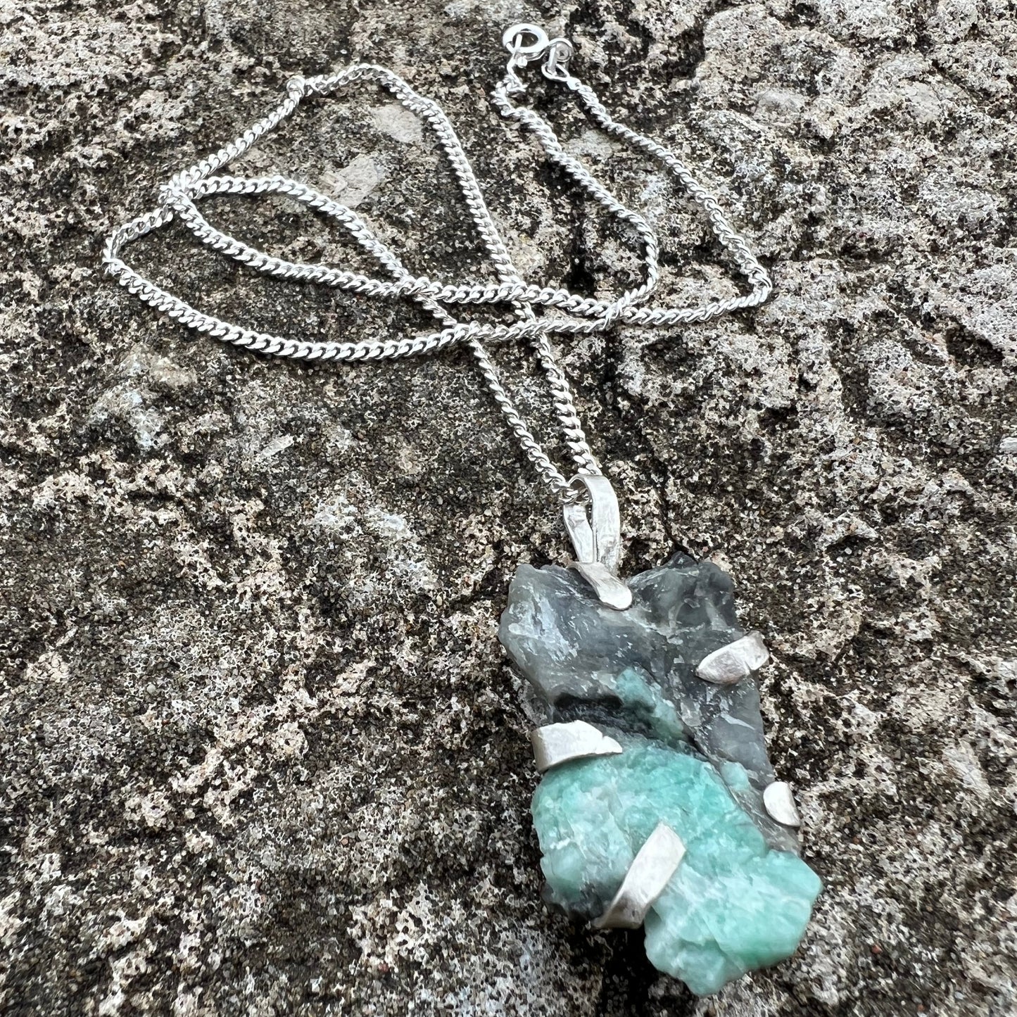 raw emerald crystal in green and black wrapped in sterlingsilver with silver chain on a textured surface