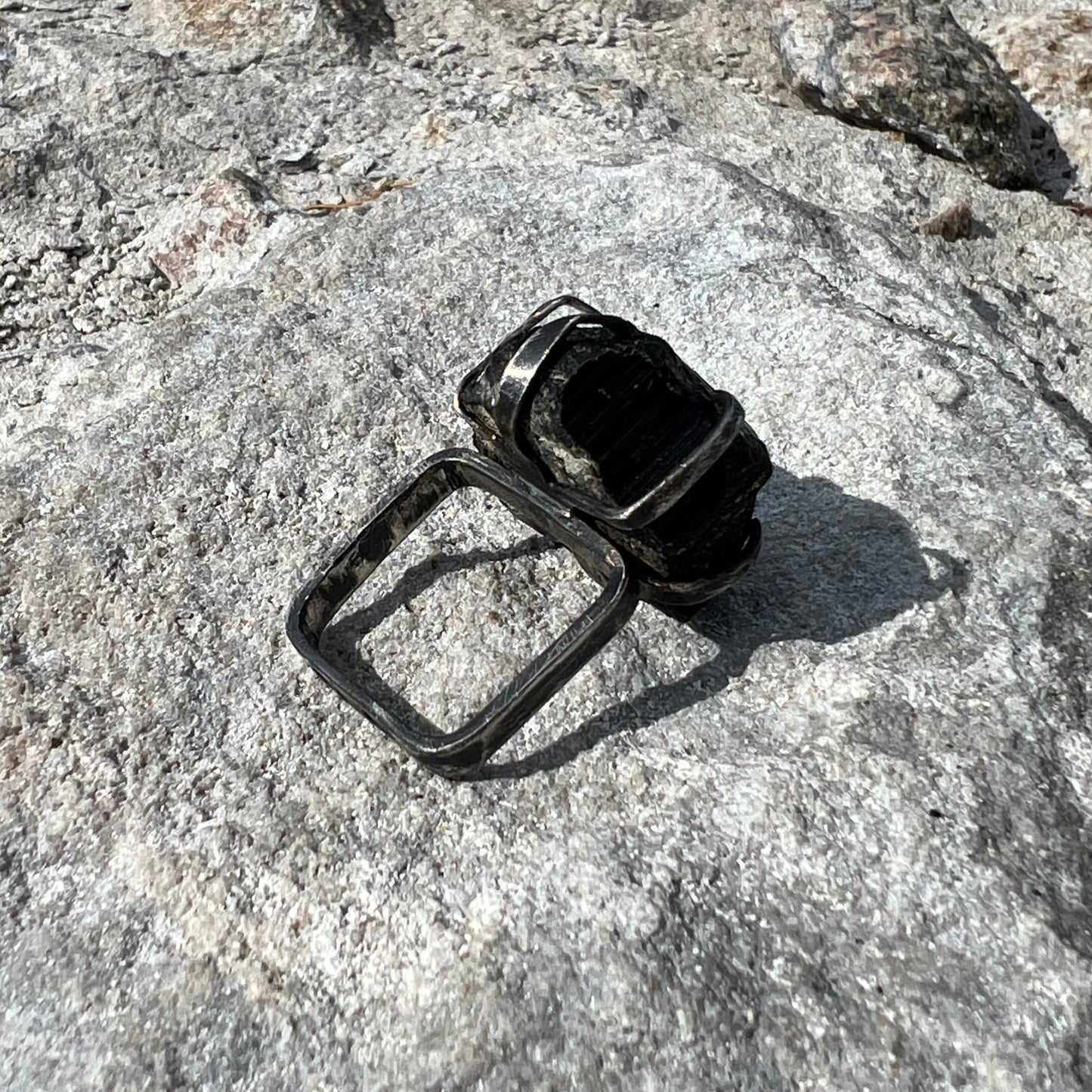 Raw Black Tourmaline crystal on a square ring band in oxidized silver on a textured stone surface