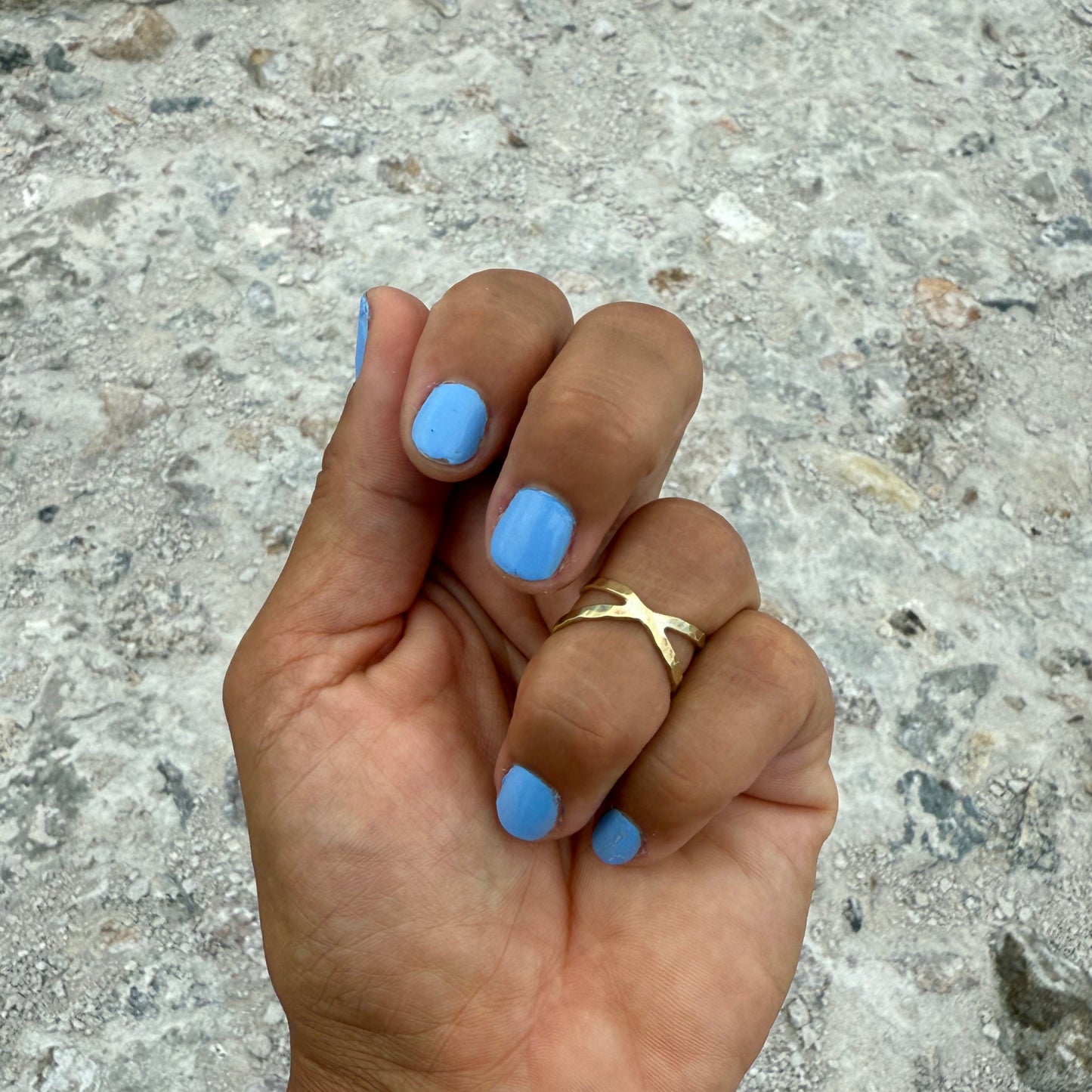 Hand with blue nail polish and a brass ring shaped like the infinity symbol on a textured stone background