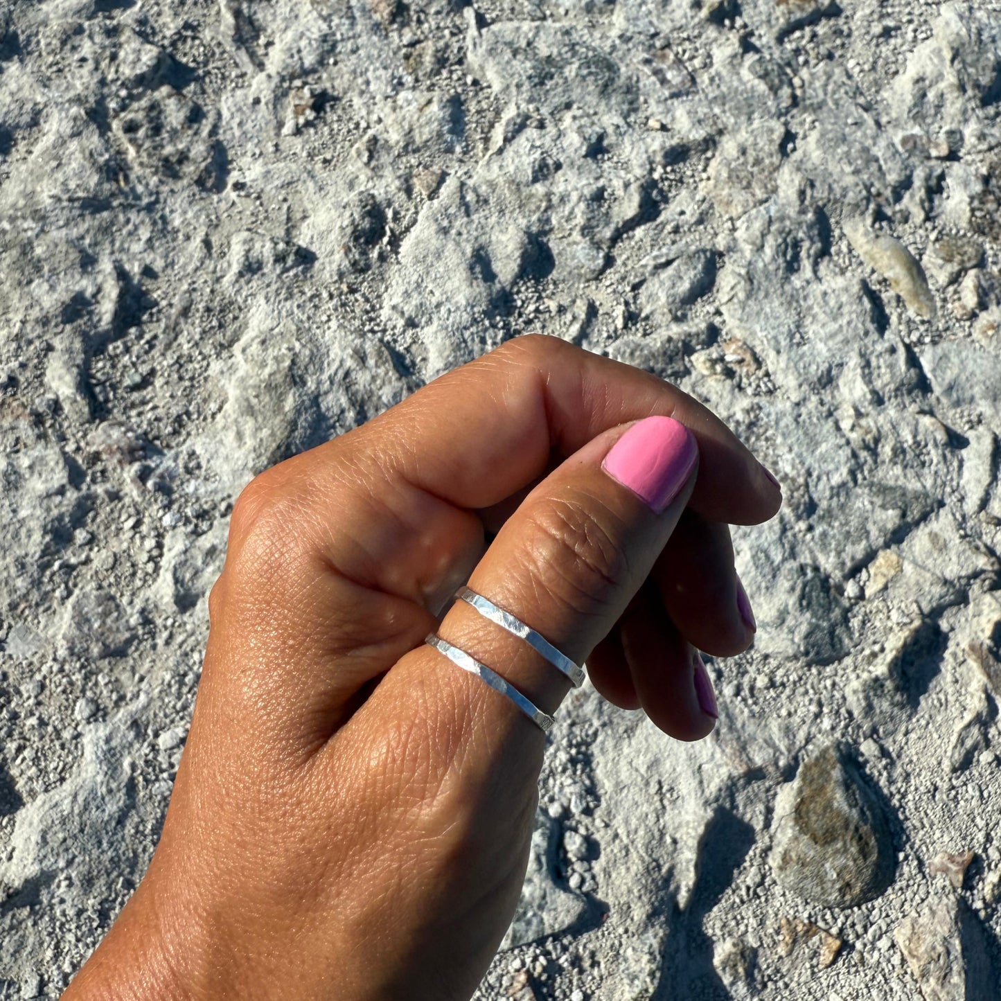 Hand with pink nail polish wearing a cross thumb ring in sterlingsilver against a textured stone background