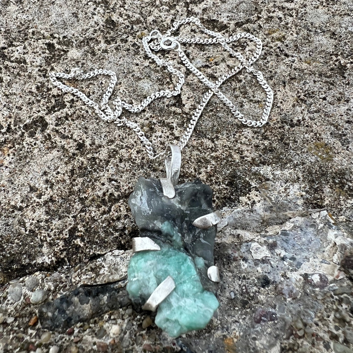 Silver chain and green gemstone on a textured stone surface