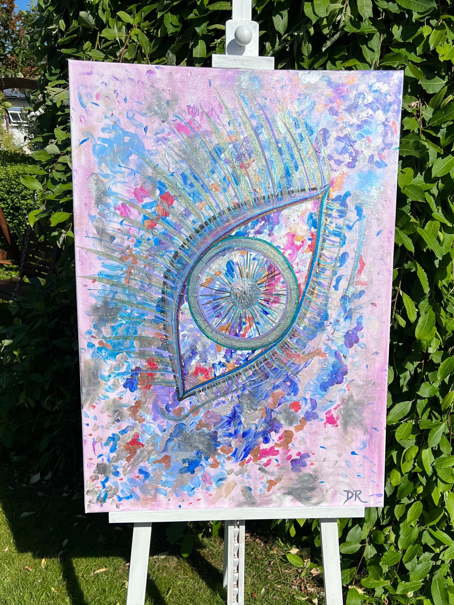 Colorful abstract artwork on a stand outdoors with greenery in the background