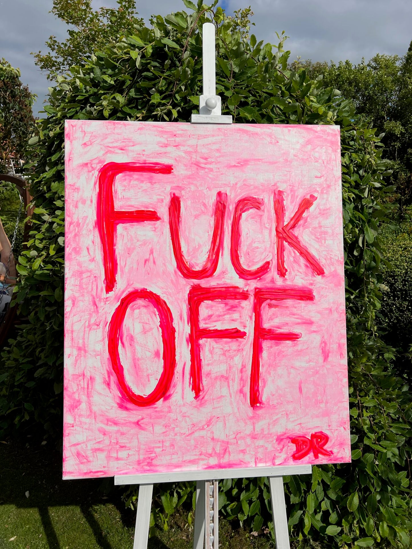 Pink painting text 'FUCK OFF' on a white stand outdoors.