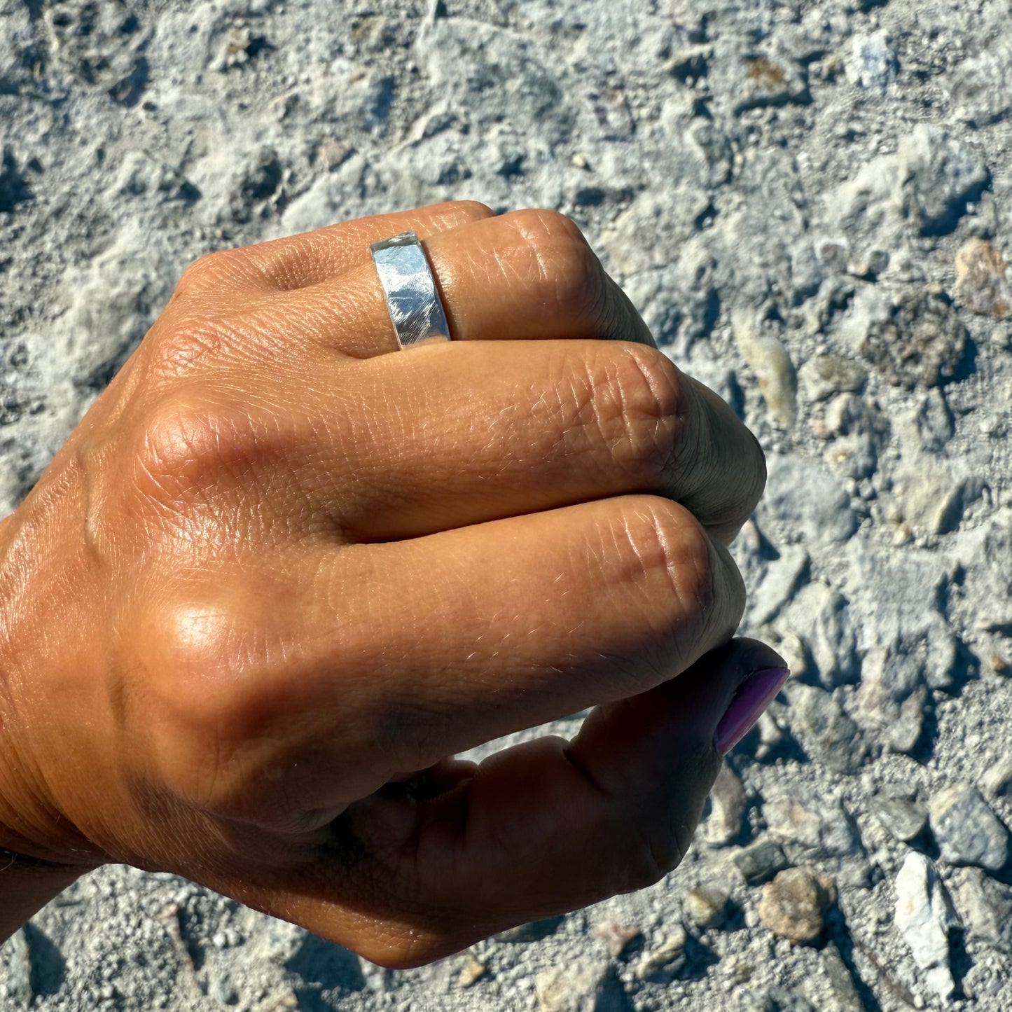 Hand with a hammered silver 925 ring on a textured stone surface