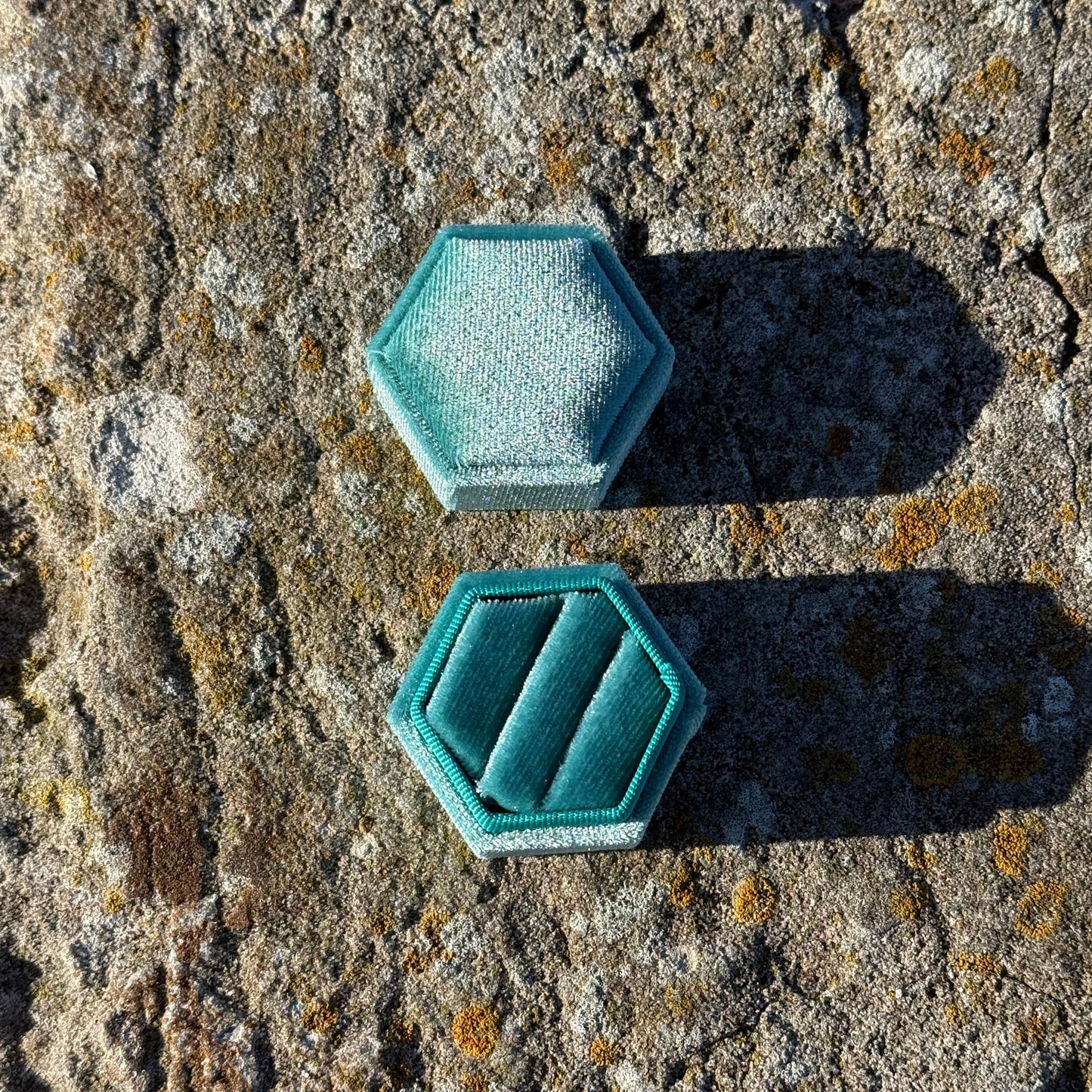 hexagonal teal velvet jewelry box on a textured stone surface