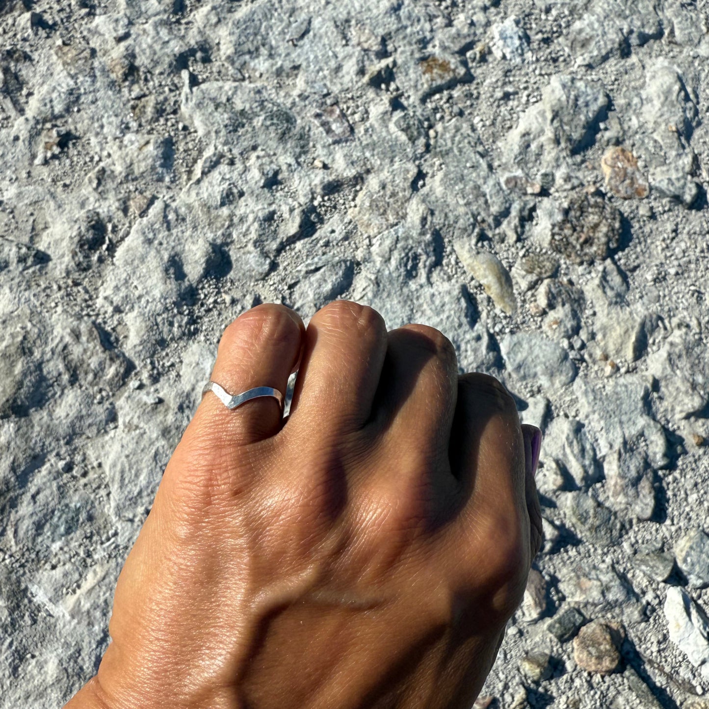 Hand with a pinky-finger-ring in silver 925 on a textured stone surface