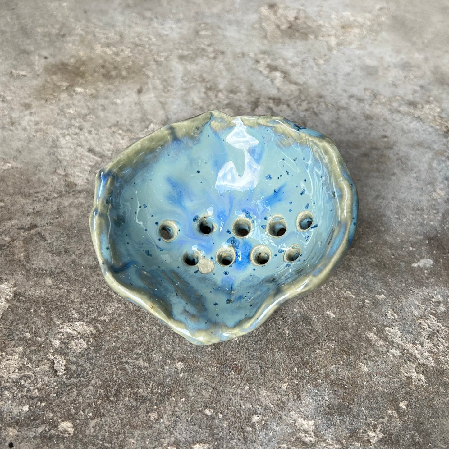 handmade one-of-a-kind Ceramic soap dish in seashell shaped form with blue glaze on a concrete surface