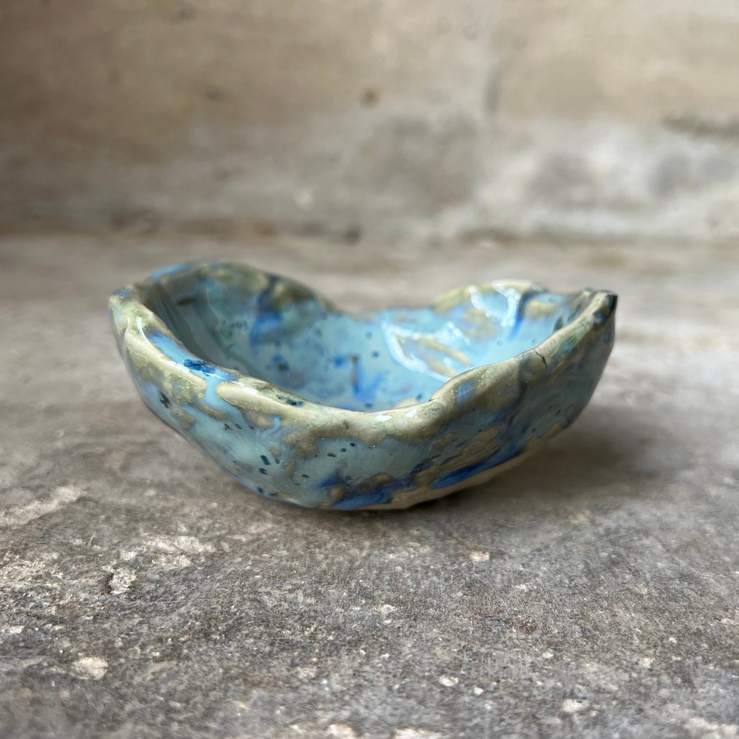 Small ceramic soap dish with blue dotted glaze on a concrete surface