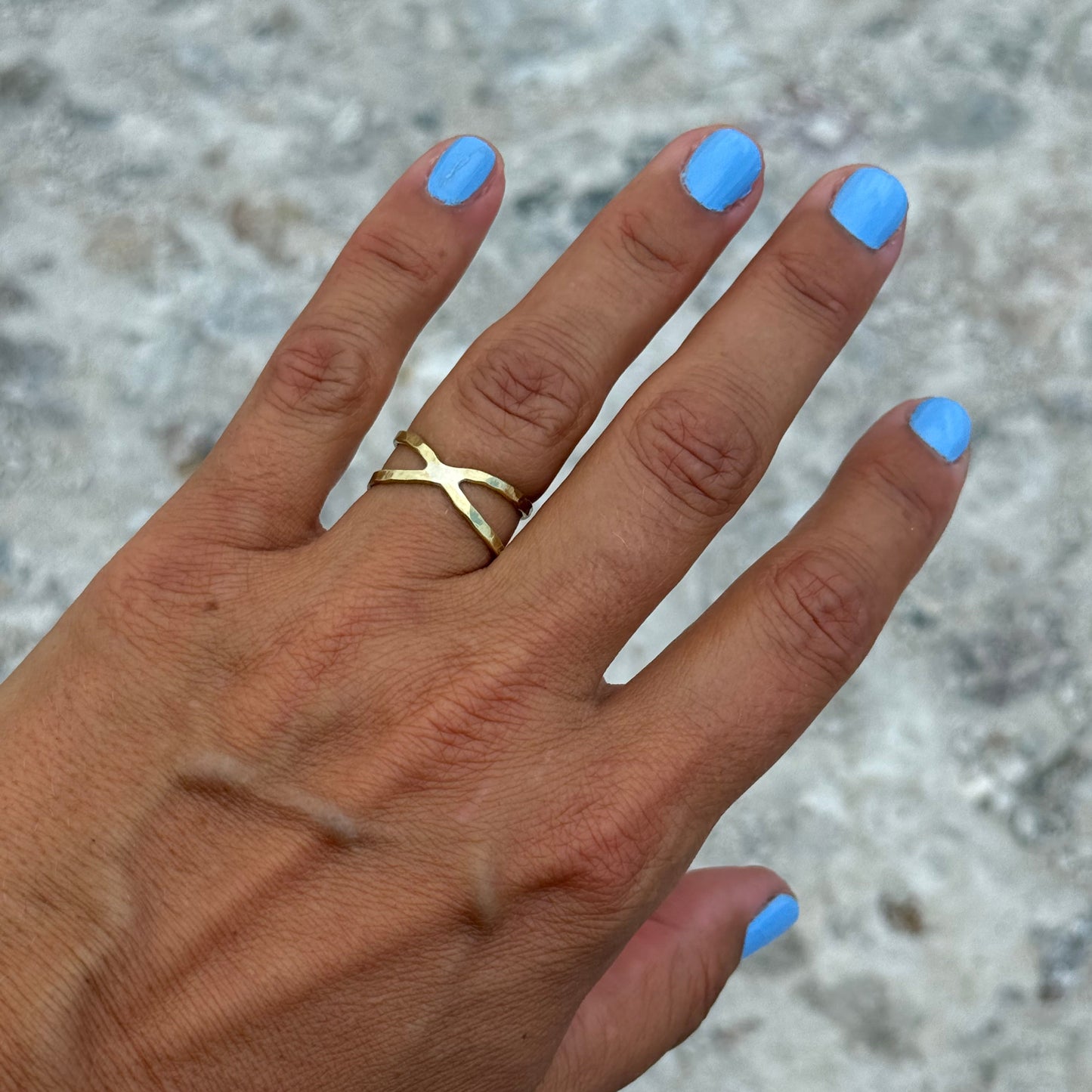 Hand with blue nail polish wearing a double band brass ring on a textured surface