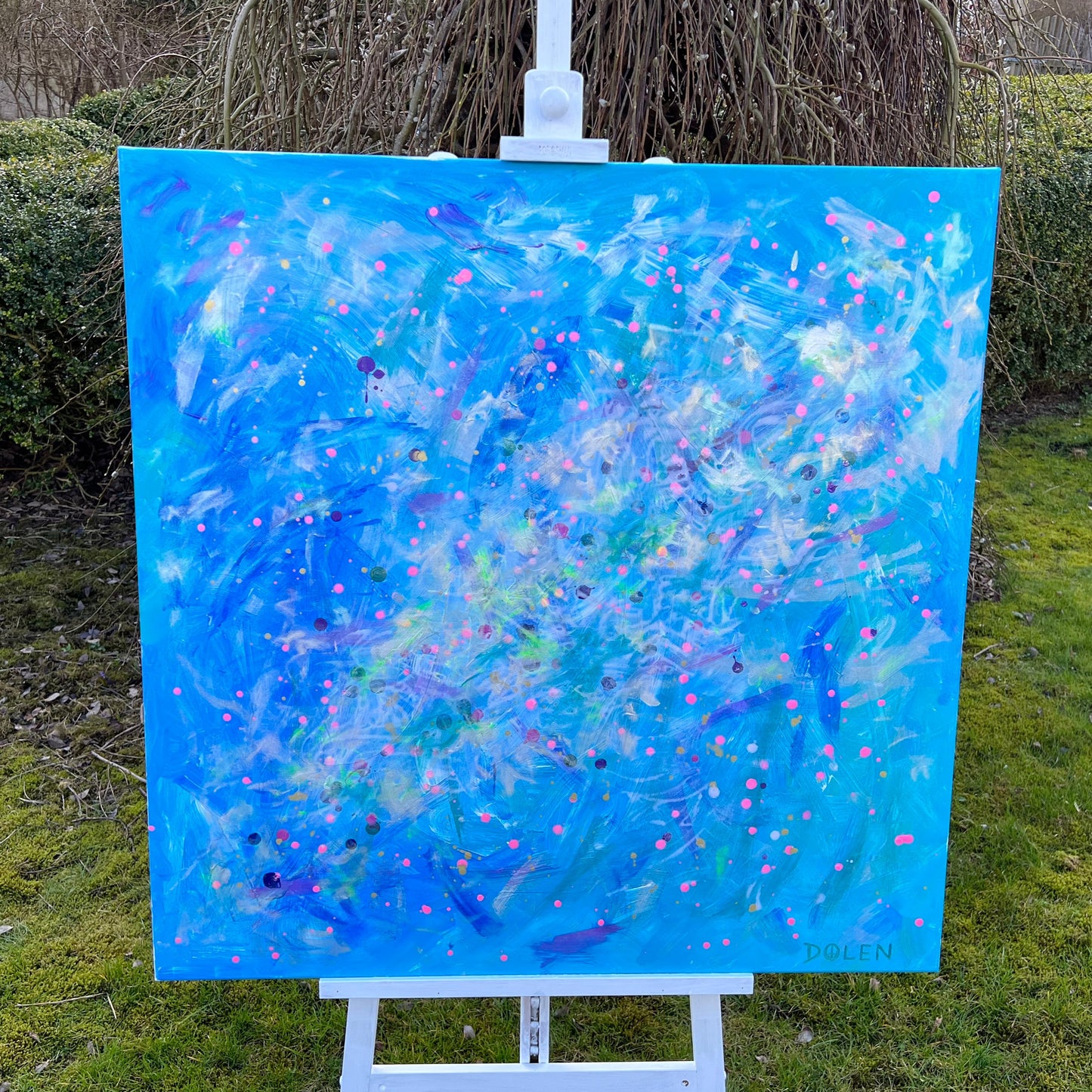 Abstract painting on an easel outdoors with greenery in the background