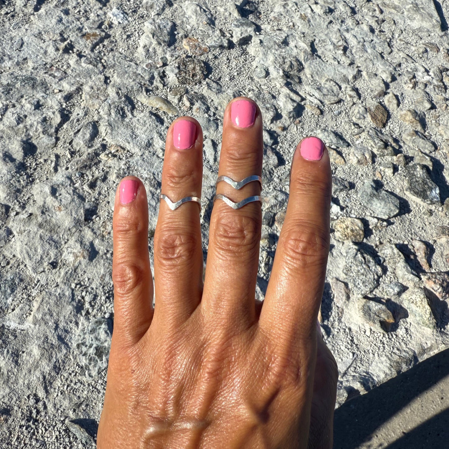 Hand with pink nail polish and upperfingerrings on a textured surface