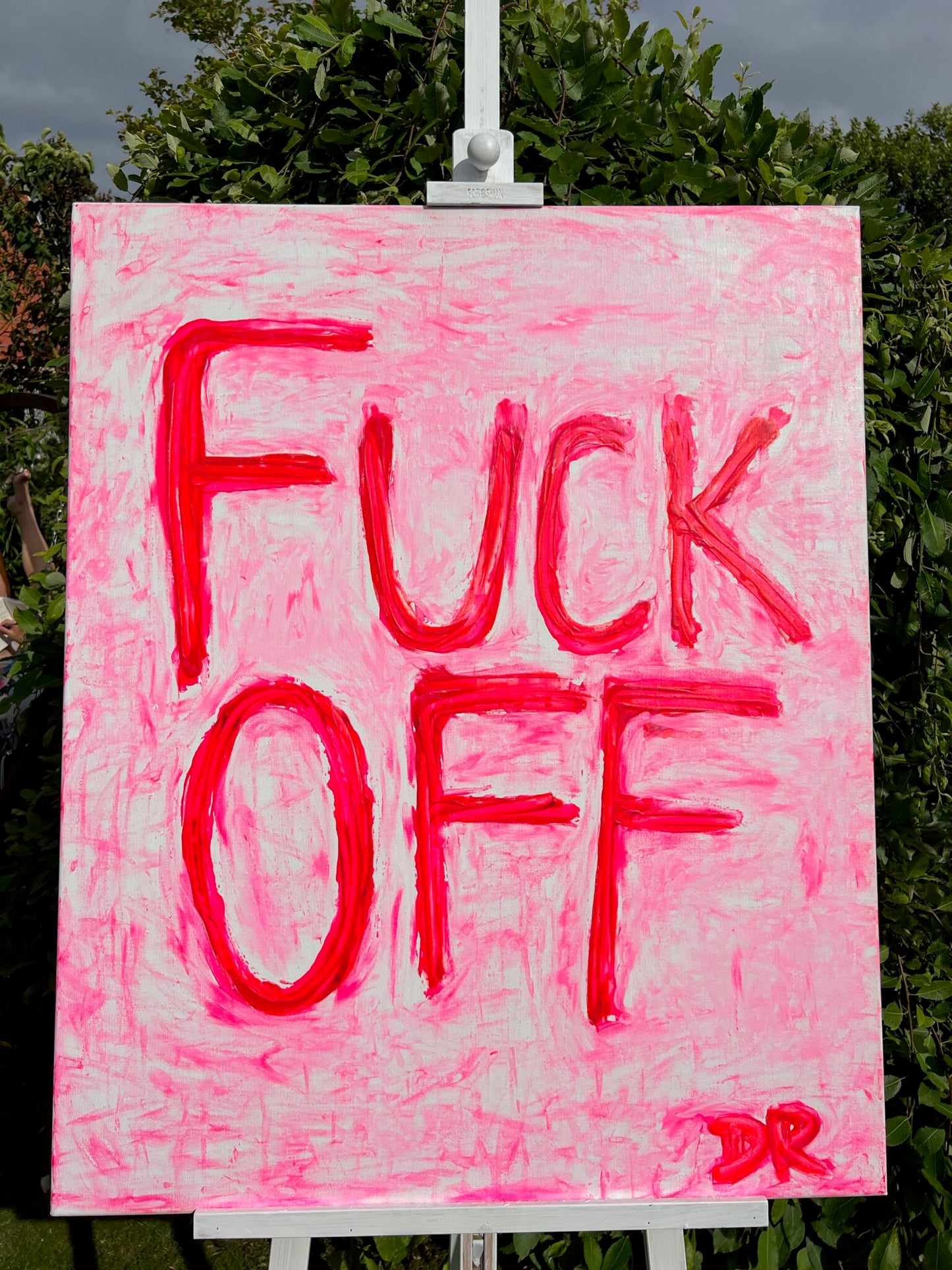 Neon Pink sign with text 'FUCK OFF' on a white stand outdoors.