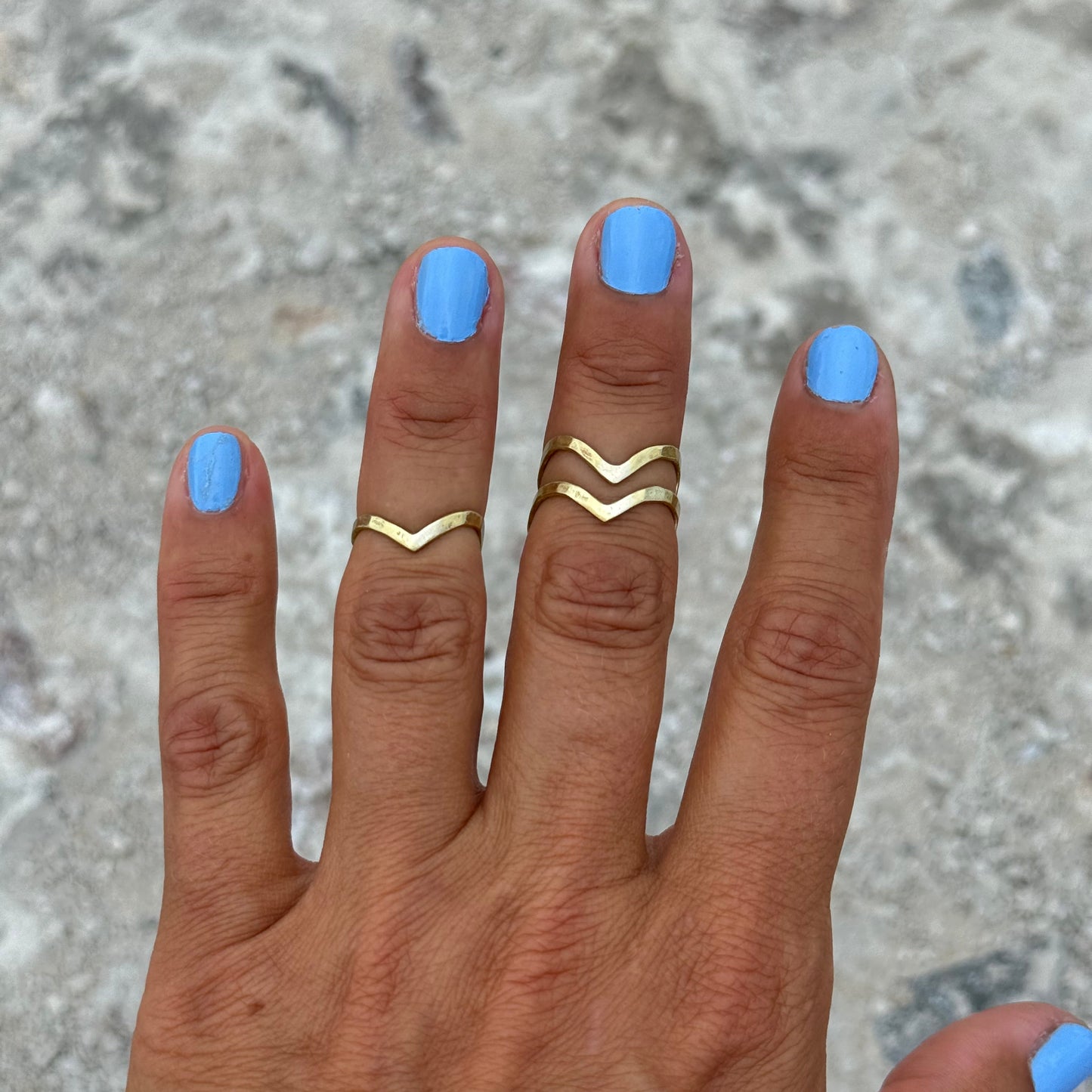 Hand with blue nail polish wearing three upperfingerrings in brass