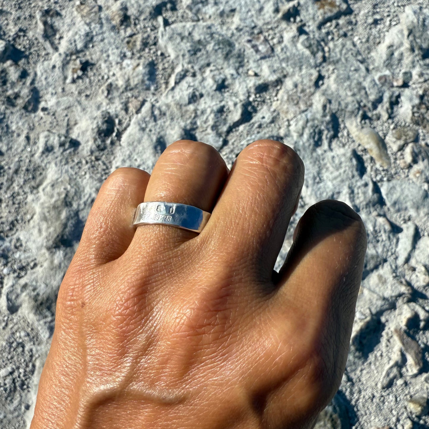 Hand with a silver ring with letters aD stamped with 925 on a textured surface