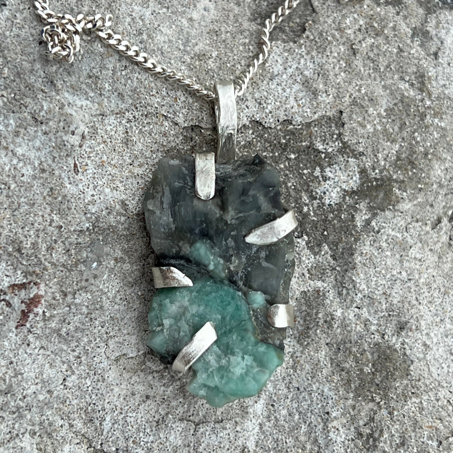 Necklace with a raw emerald in sterlingsilver pendant on a textured surface