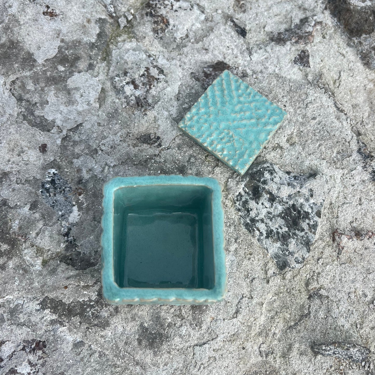 Turquoise ceramic box with lid on a textured stone surface