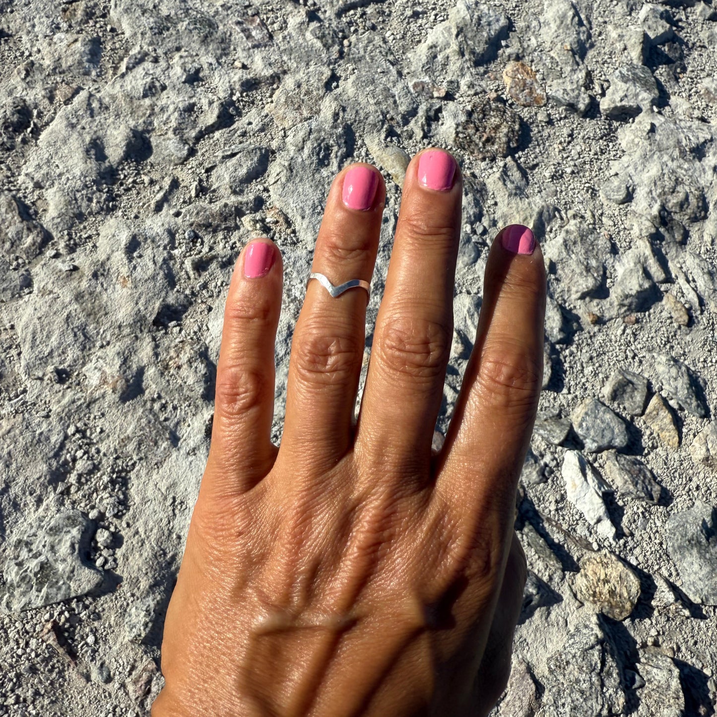Hand with pink nail polish and a hammered half-finger-ring in sterling silver on a textured stone surface