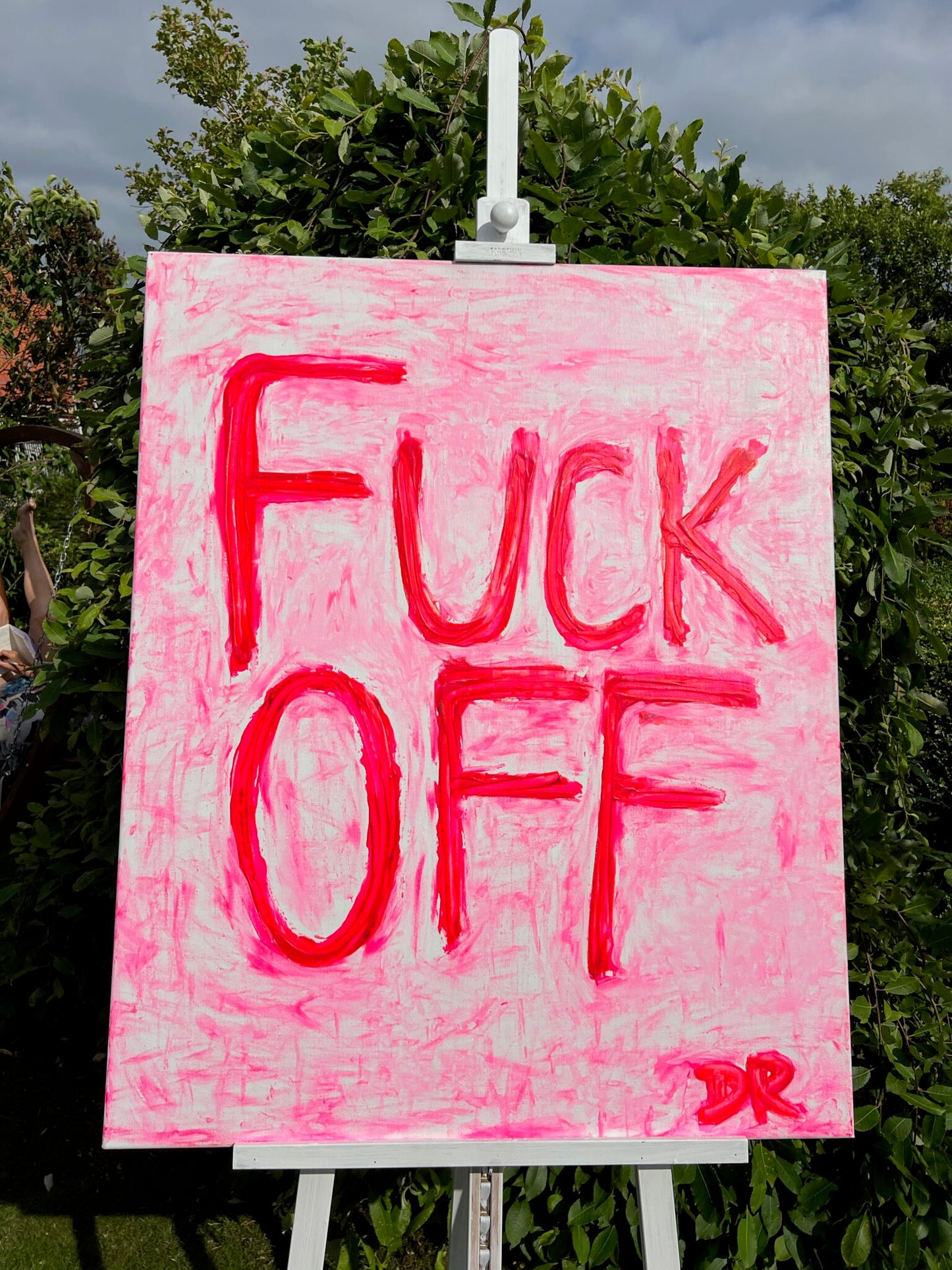 textured acrylic painting on canvas with neonpink text 'FUCK OFF' on a white easel outdoors.
