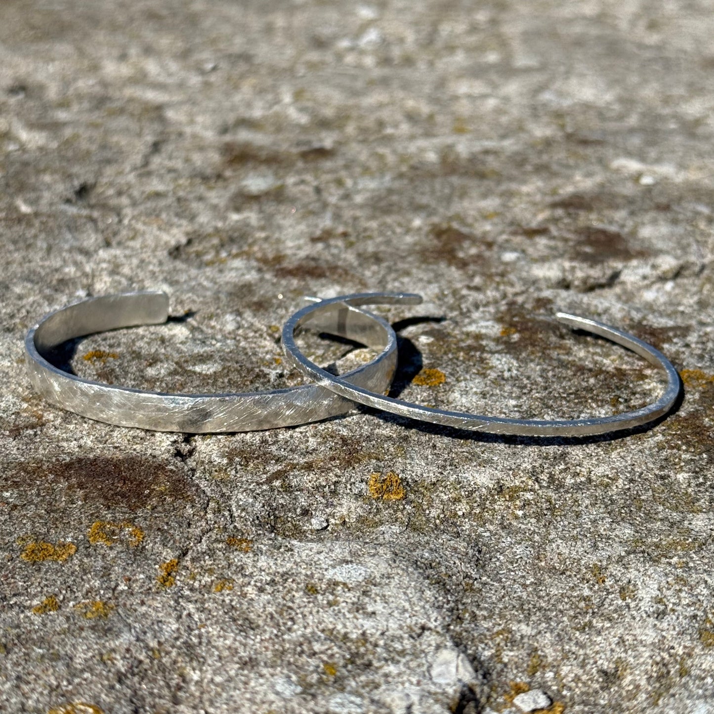 Thick and thin silver cuff bracelets on a textured stone surface