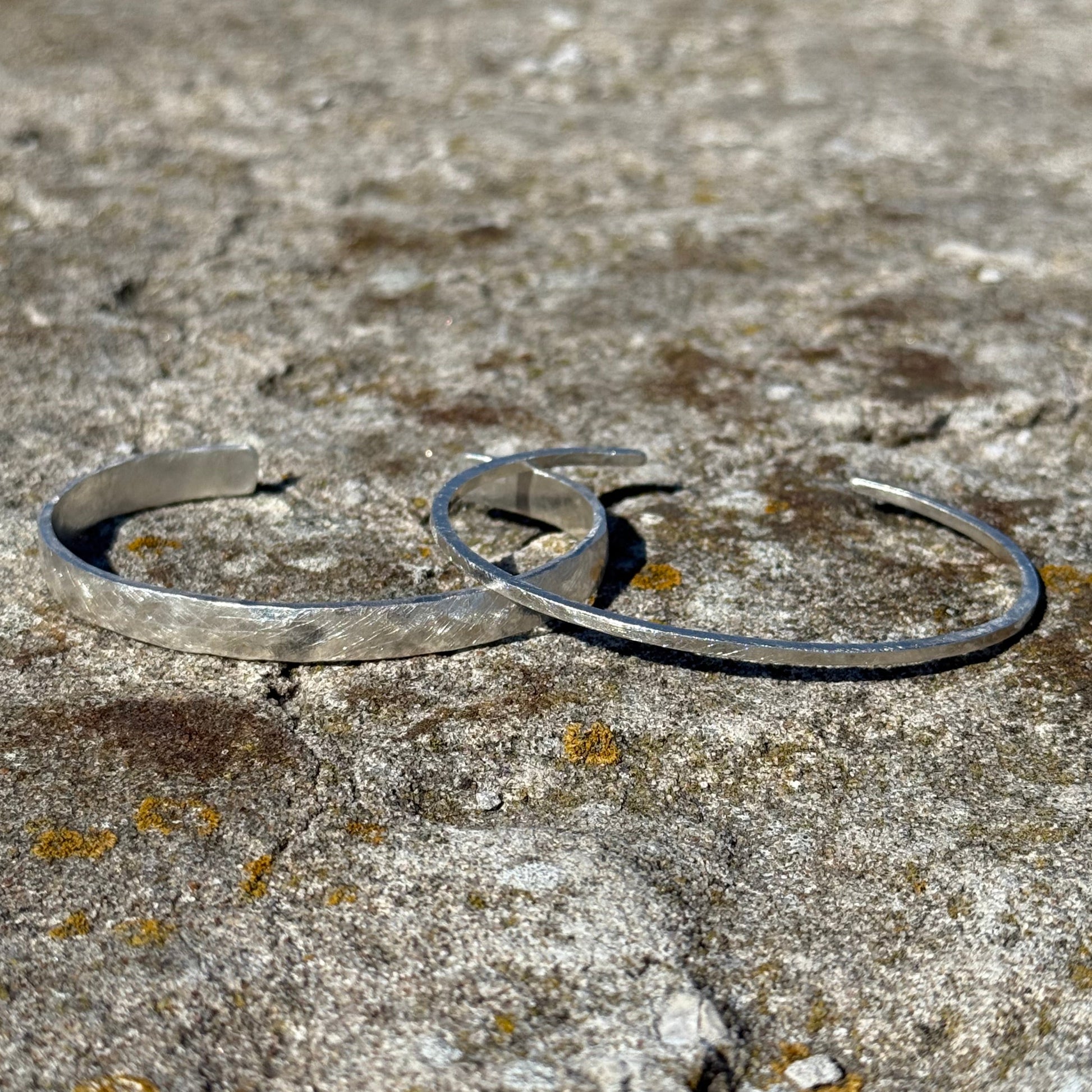 Thick and thin silver cuff bracelets on a textured stone surface