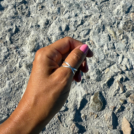 Hand with pink nail polish wearing a silver ring on a textured stone surface