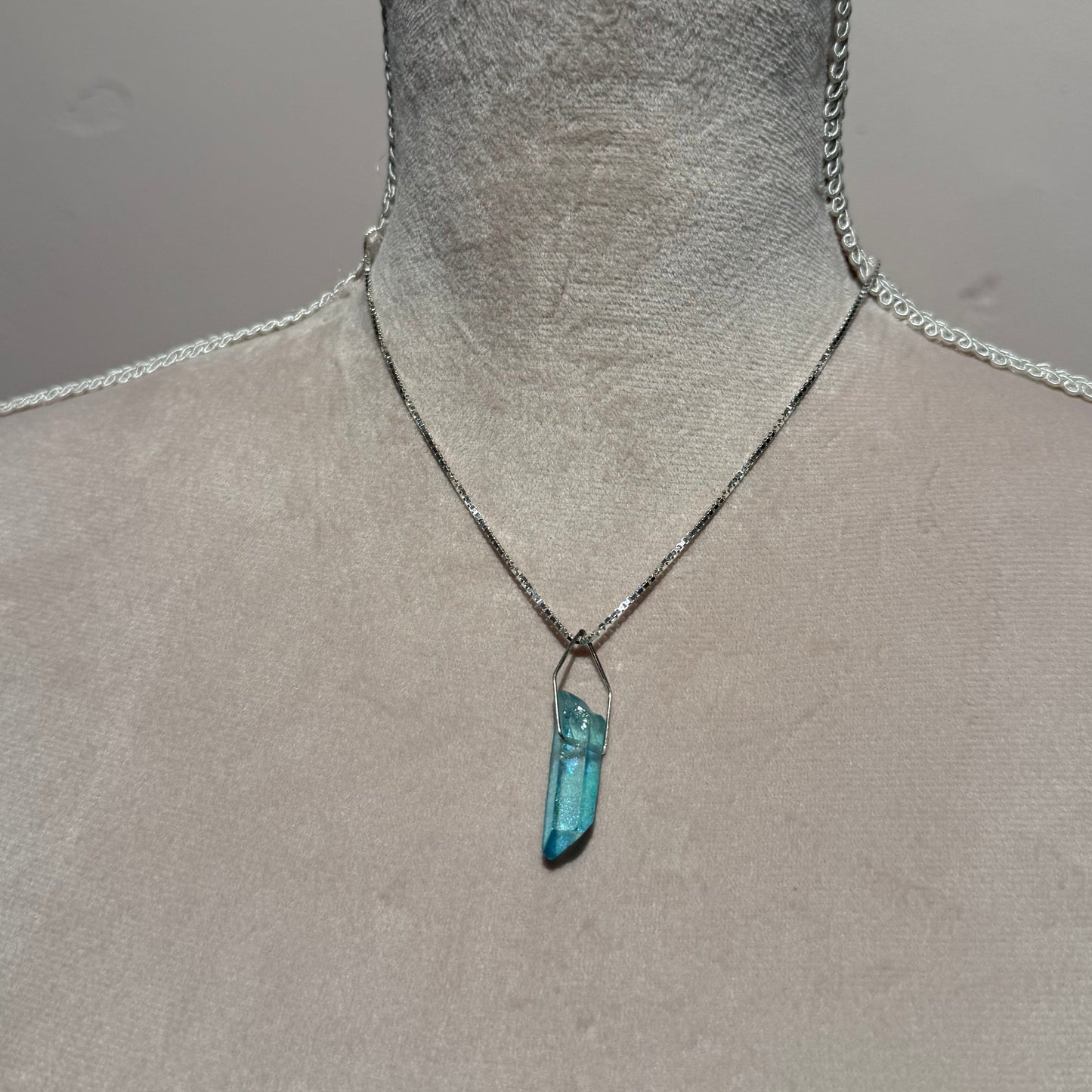 Close-up of a textured surface with a VENEZIA silver chain and a small aqua. blue titanium quartz pendant.