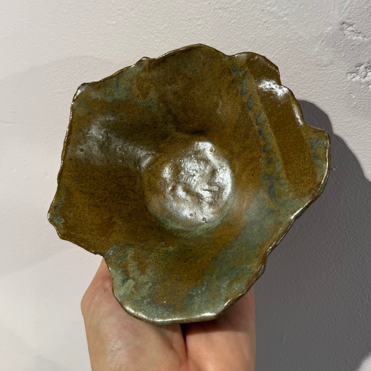Hand holding a greenish-brown ceramic bowl against a light background