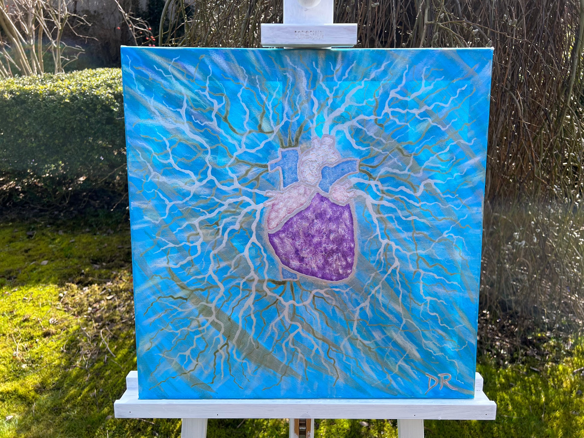 Painting of a stylized heart on a blue background, displayed on an easel outdoors.