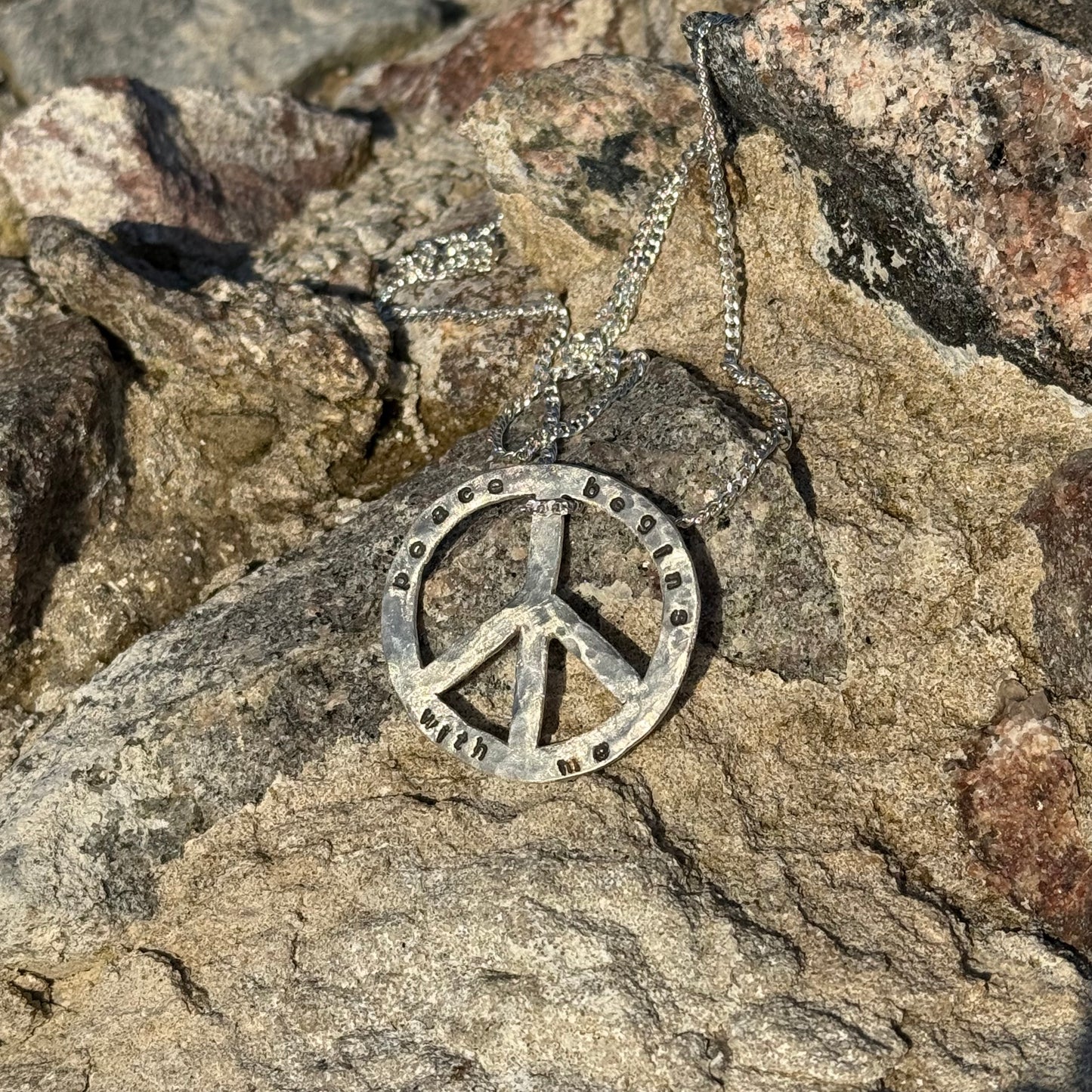 Silver peace symbol necklace on a rocky surface