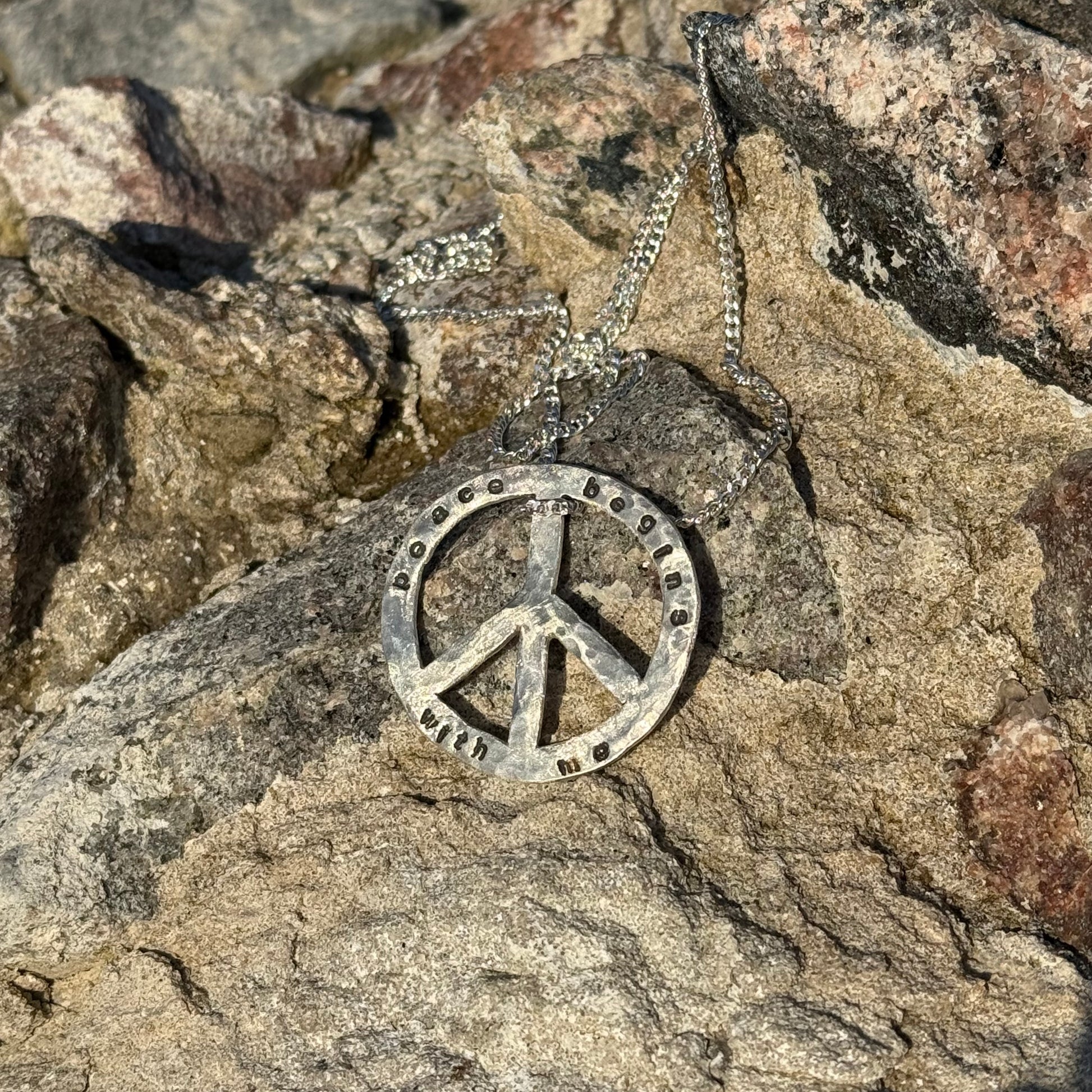 Silver peace symbol necklace on a rocky surface