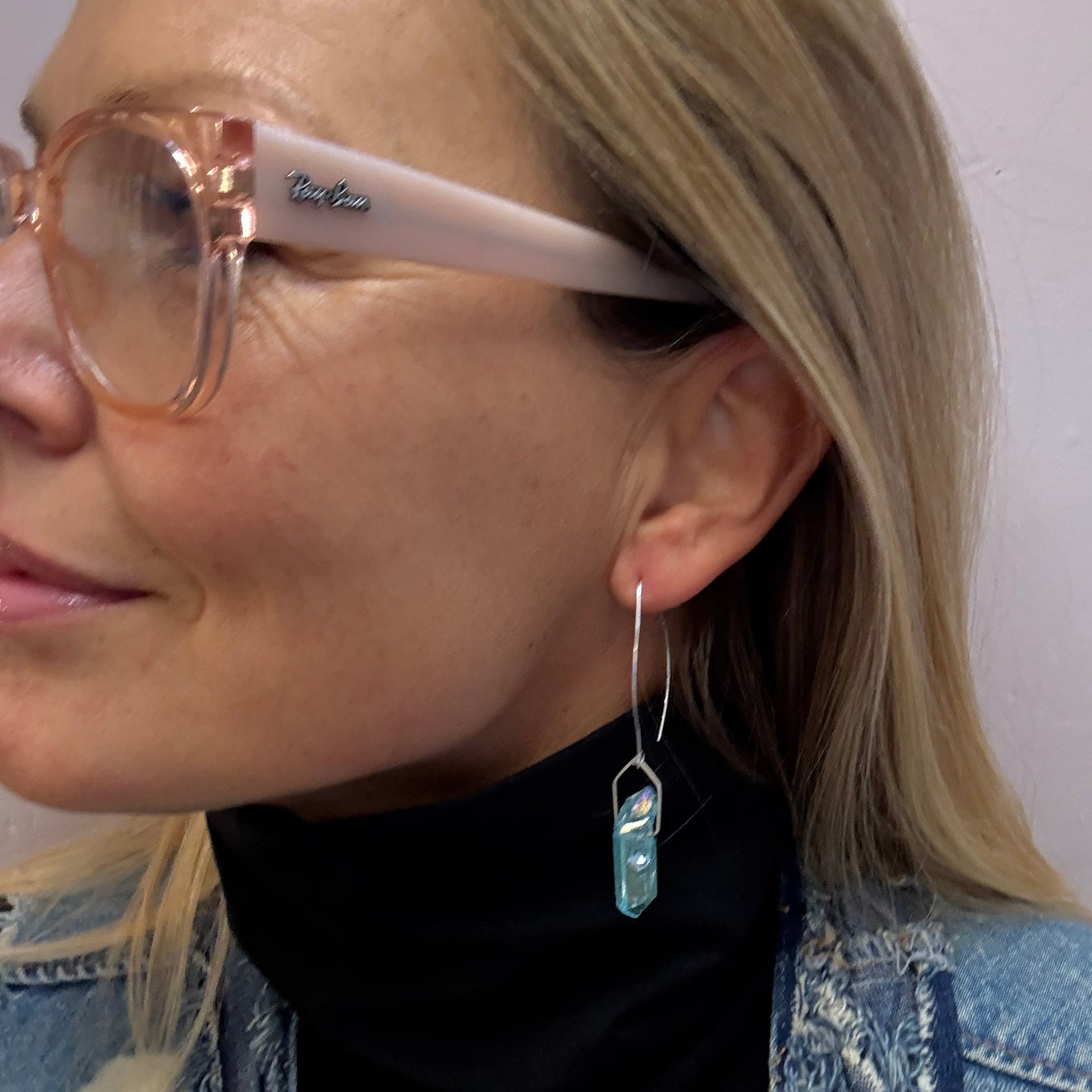 Person wearing a aqua blue titanium quartz silver eearrings, with glasses on a white background.