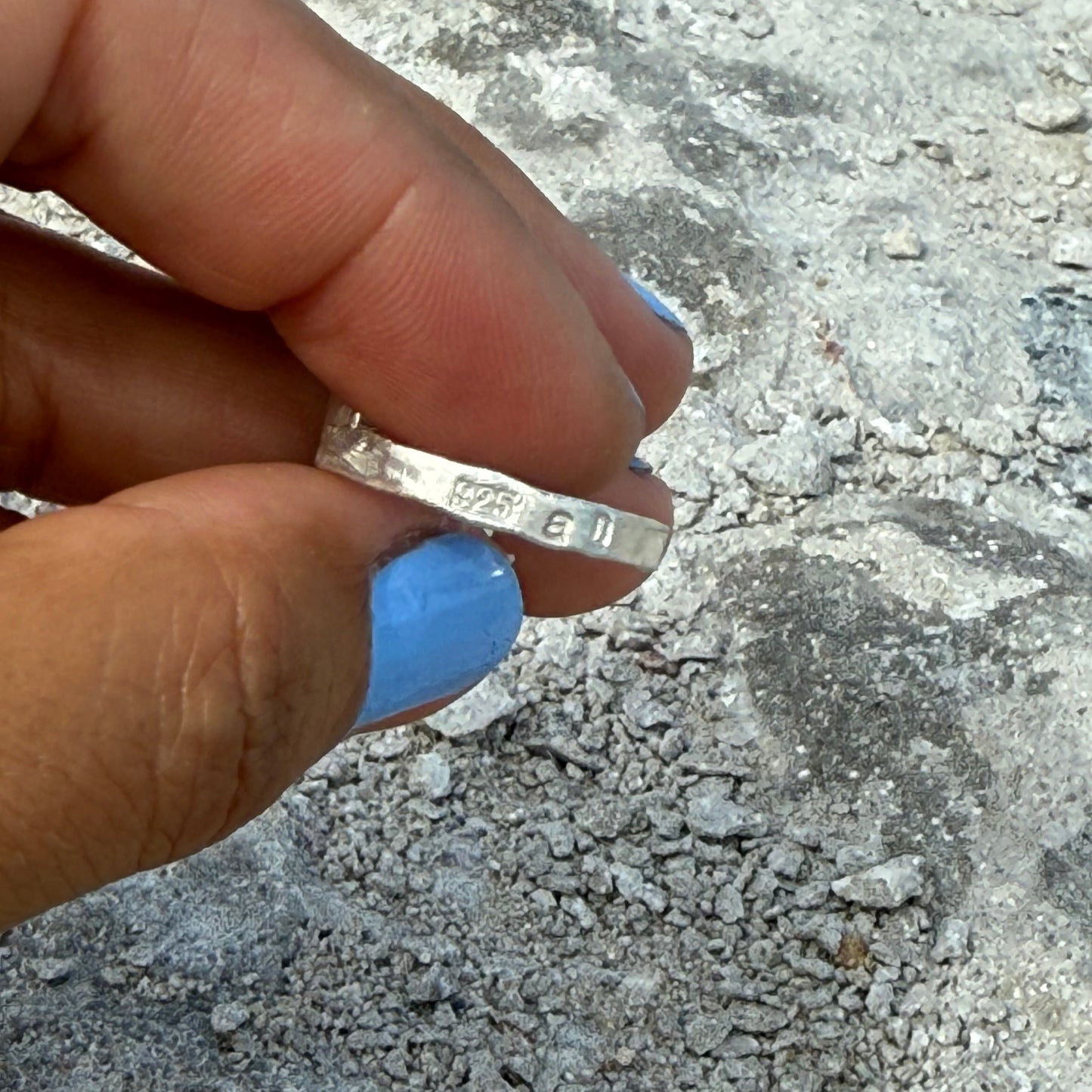 925 stamped on a hammered sterling silver ring ring held between fingers with a textured gray background