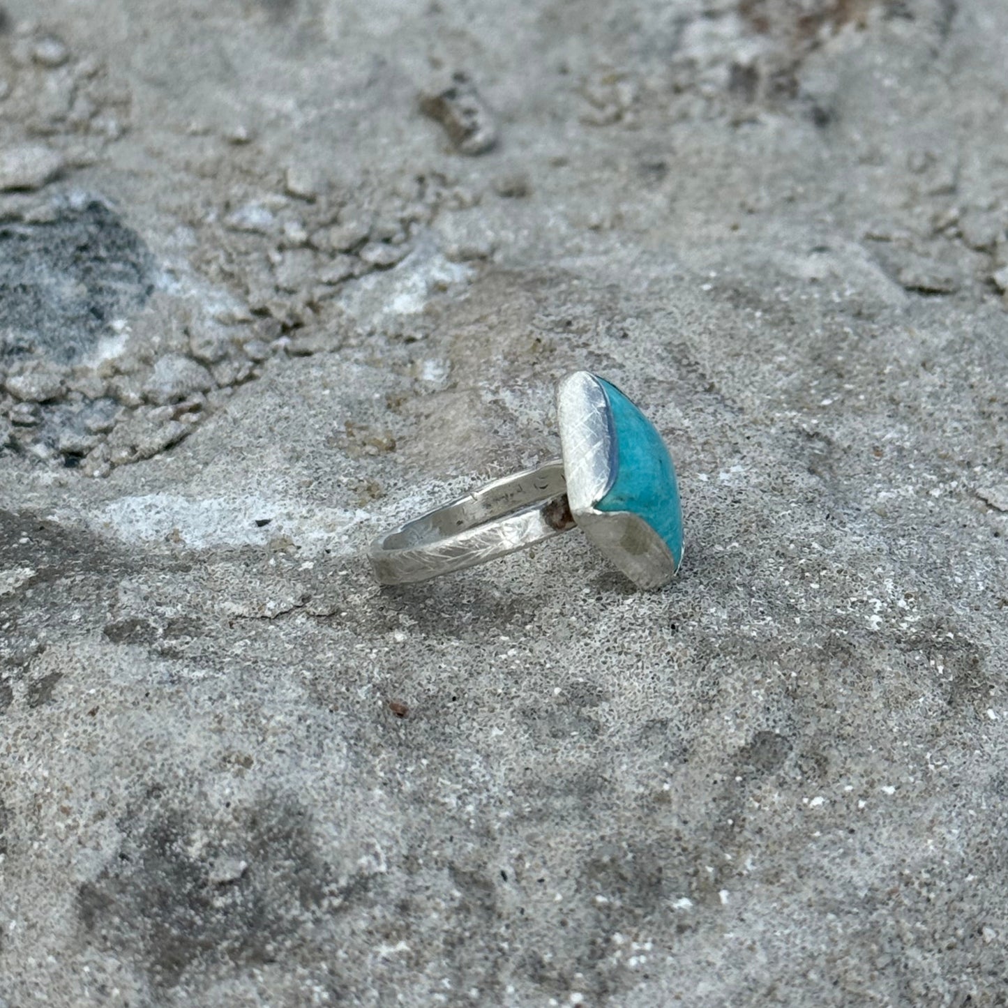Silver ring with a blue stone on sandy ground