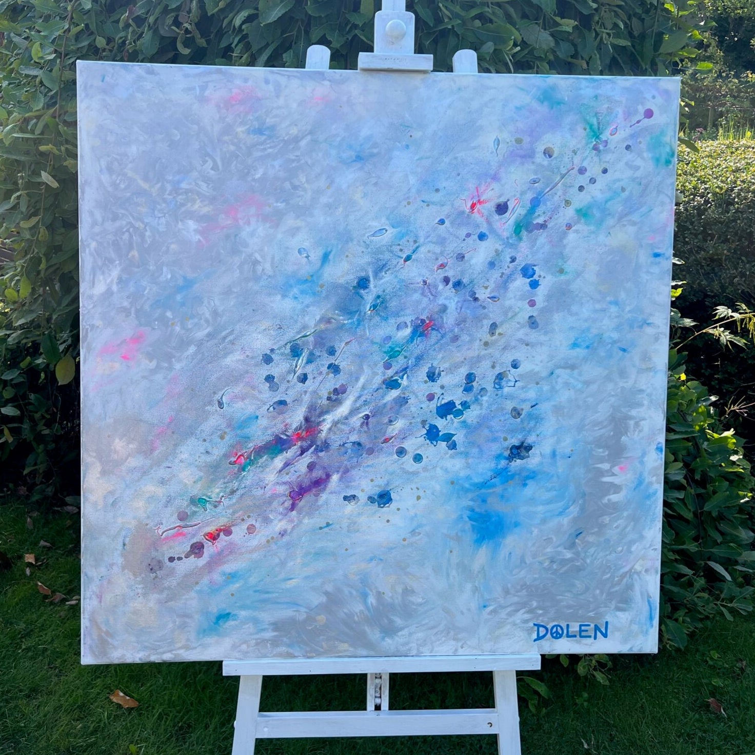 Abstract painting of a galaxy on an easel outdoors with greenery in the background