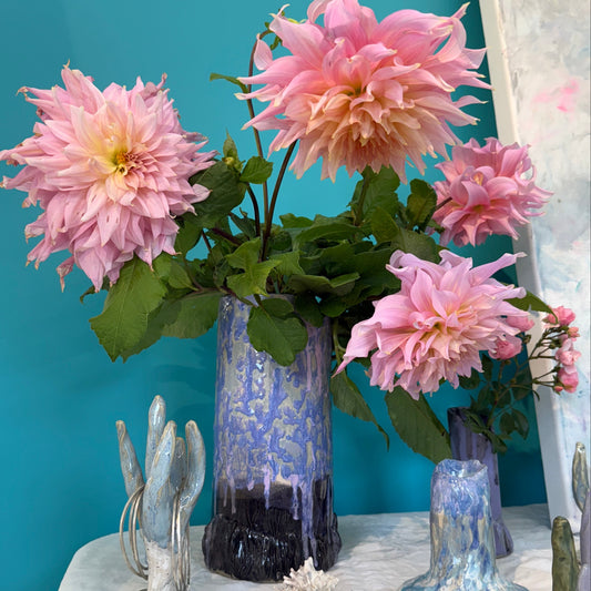 Pink flowers in a handmade ceramics vase with blue, pink and black glazing on a blue surface with decorative elements
