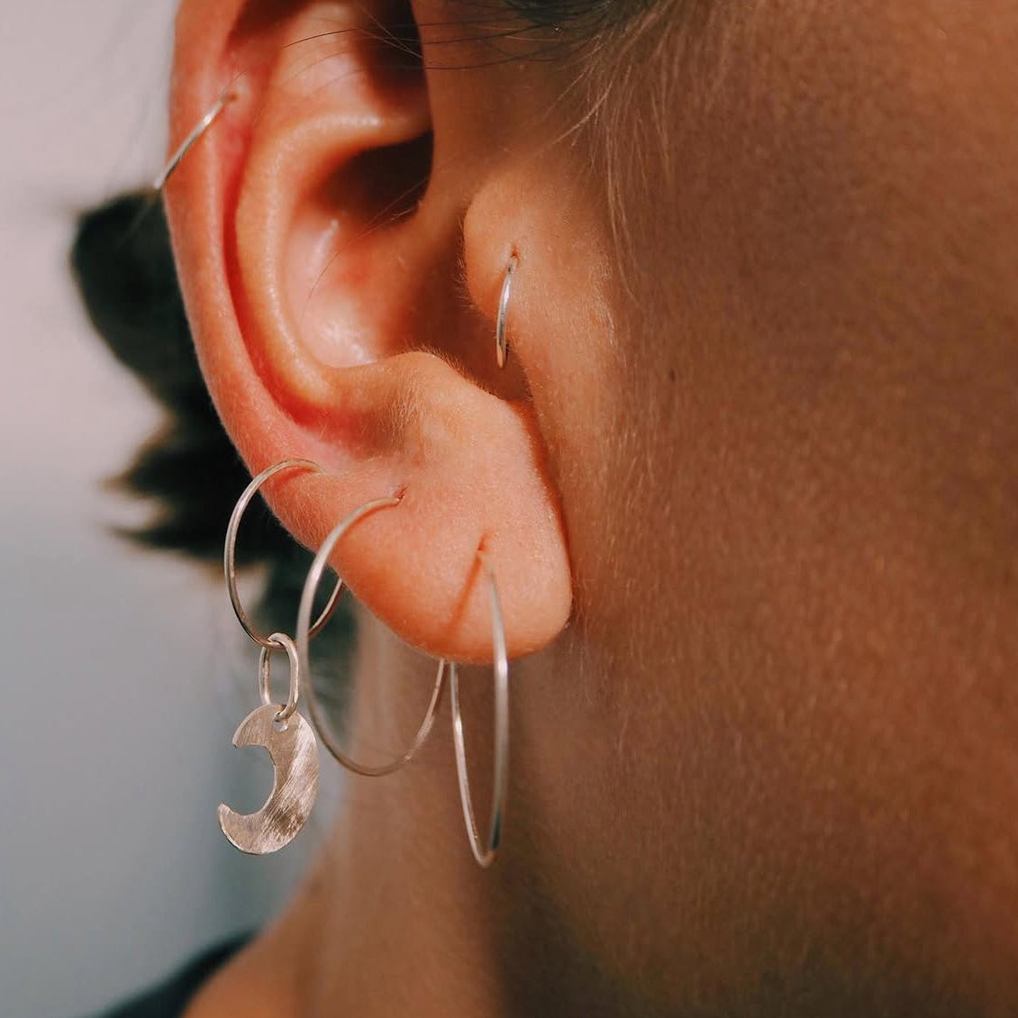 Close-up of an ear wearing silver hoop earrings with a silver moon charm
