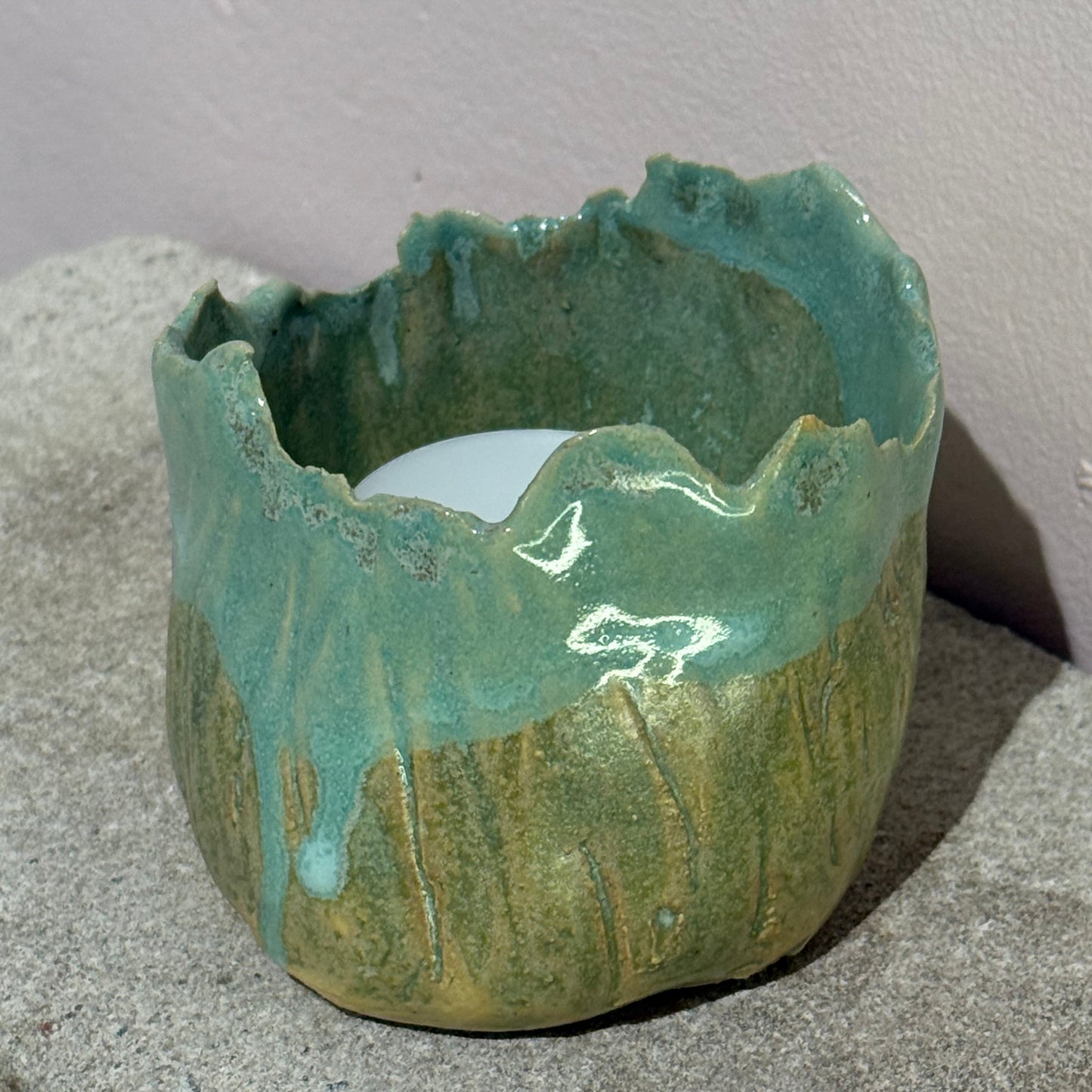 green ceramic candle holder on concrete surface with a soft pink background