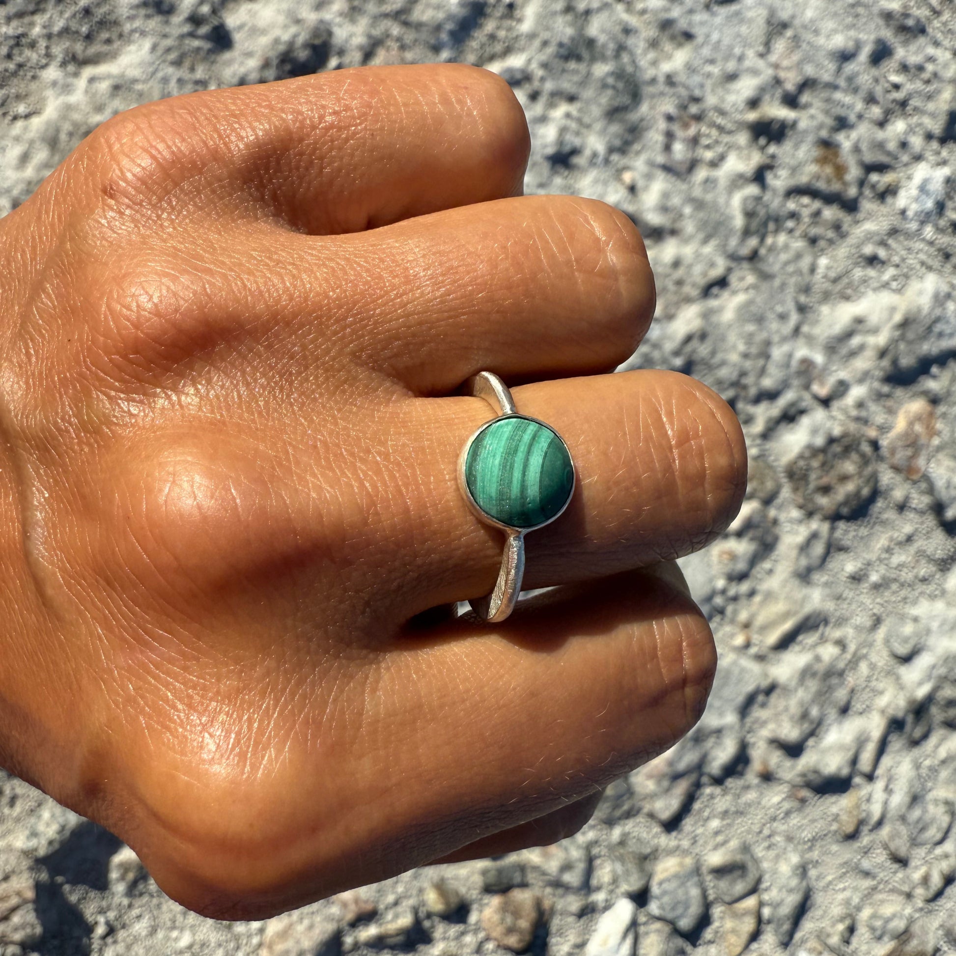 Hand wearing a ring with a green malachite gemstone silverring on a textured surface