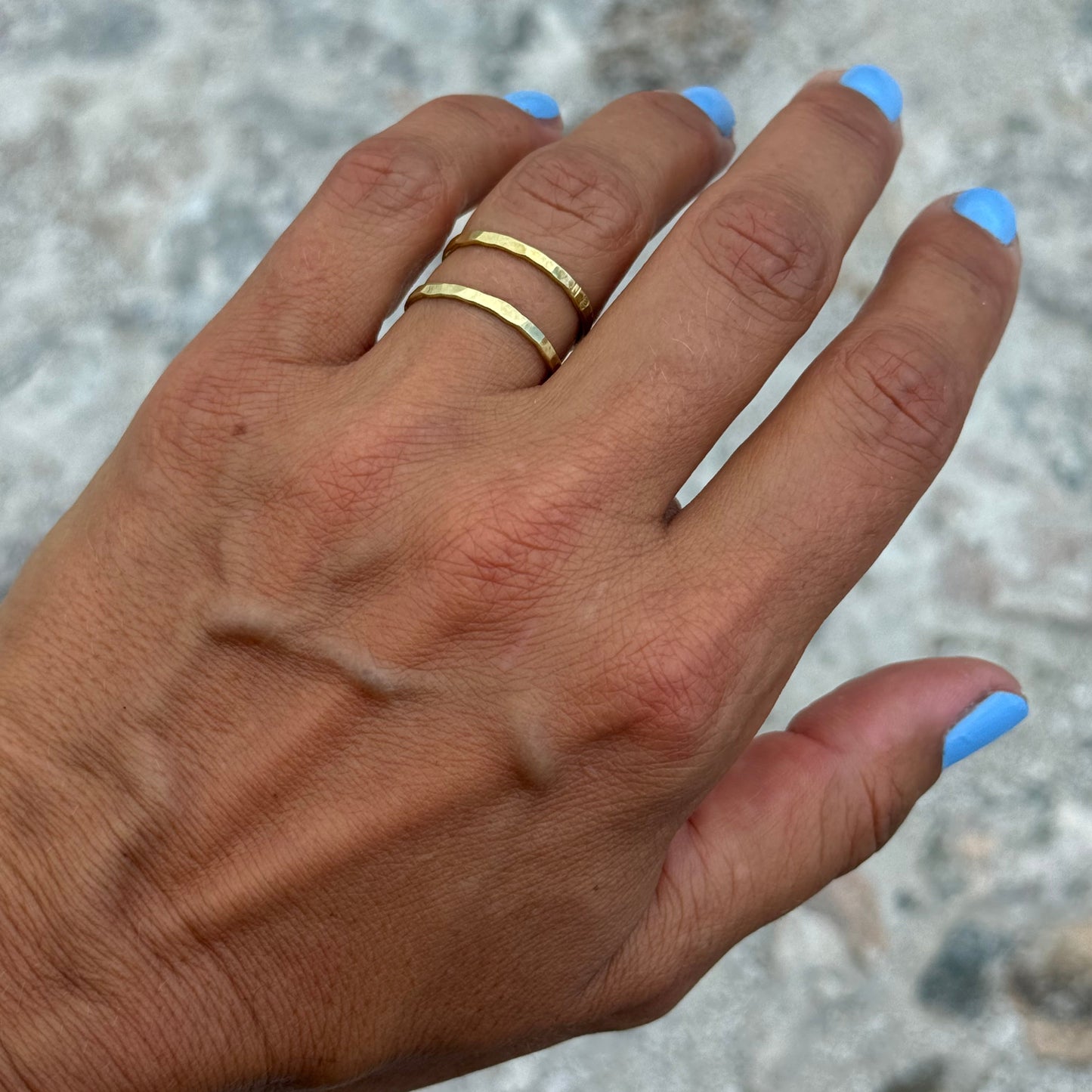 Hand with double brass ring and blue nail polish on a textured surface