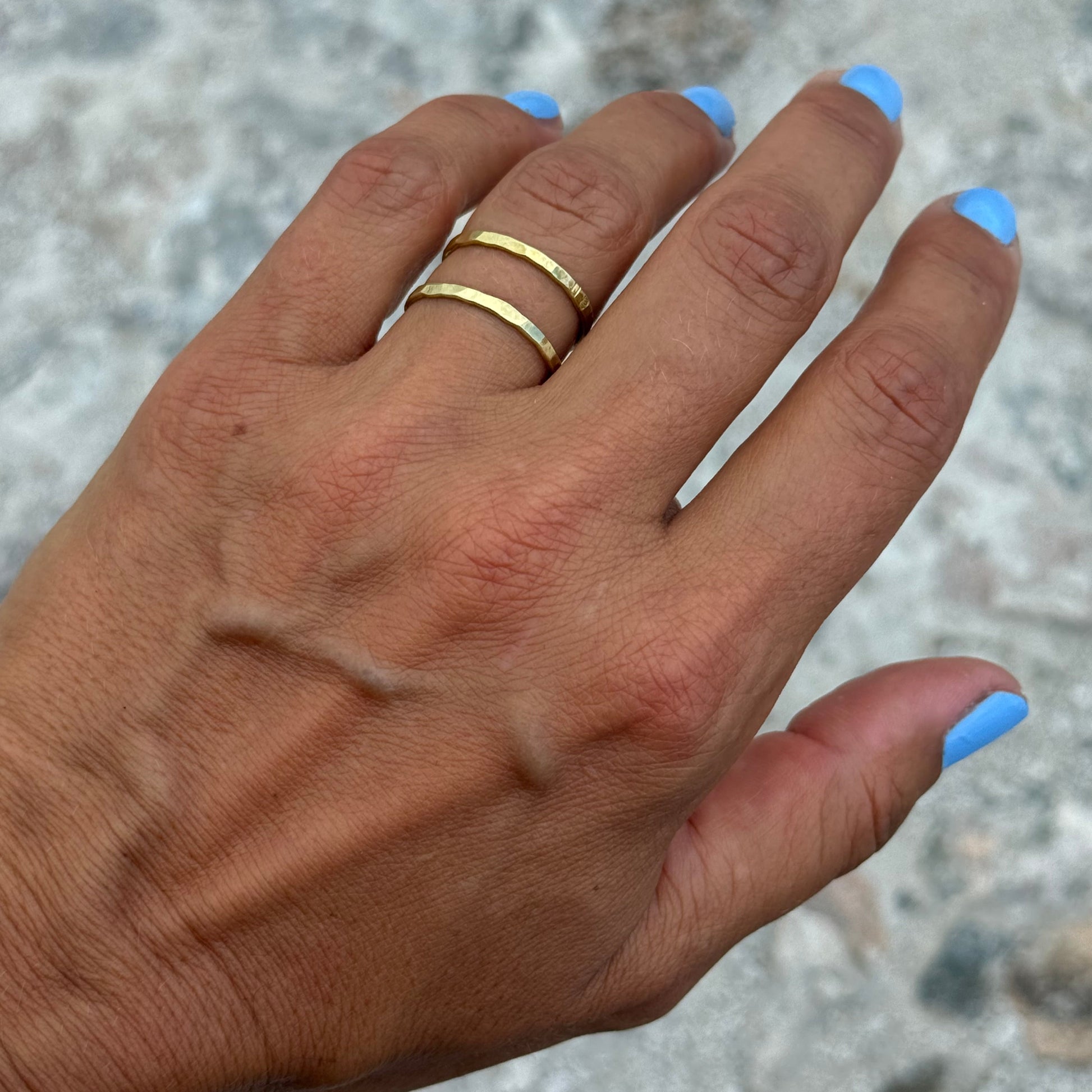 Hand with double brass ring and blue nail polish on a textured surface