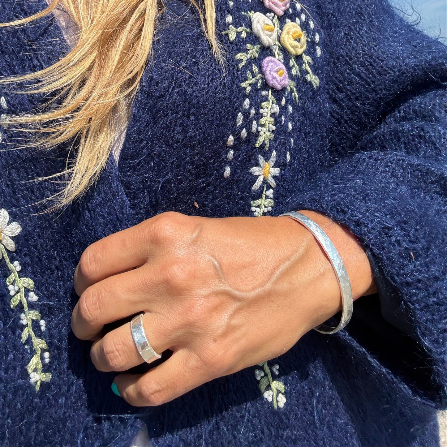 Person wearing a blue garment with floral embroidery wnd silveer cuff and silvere ring