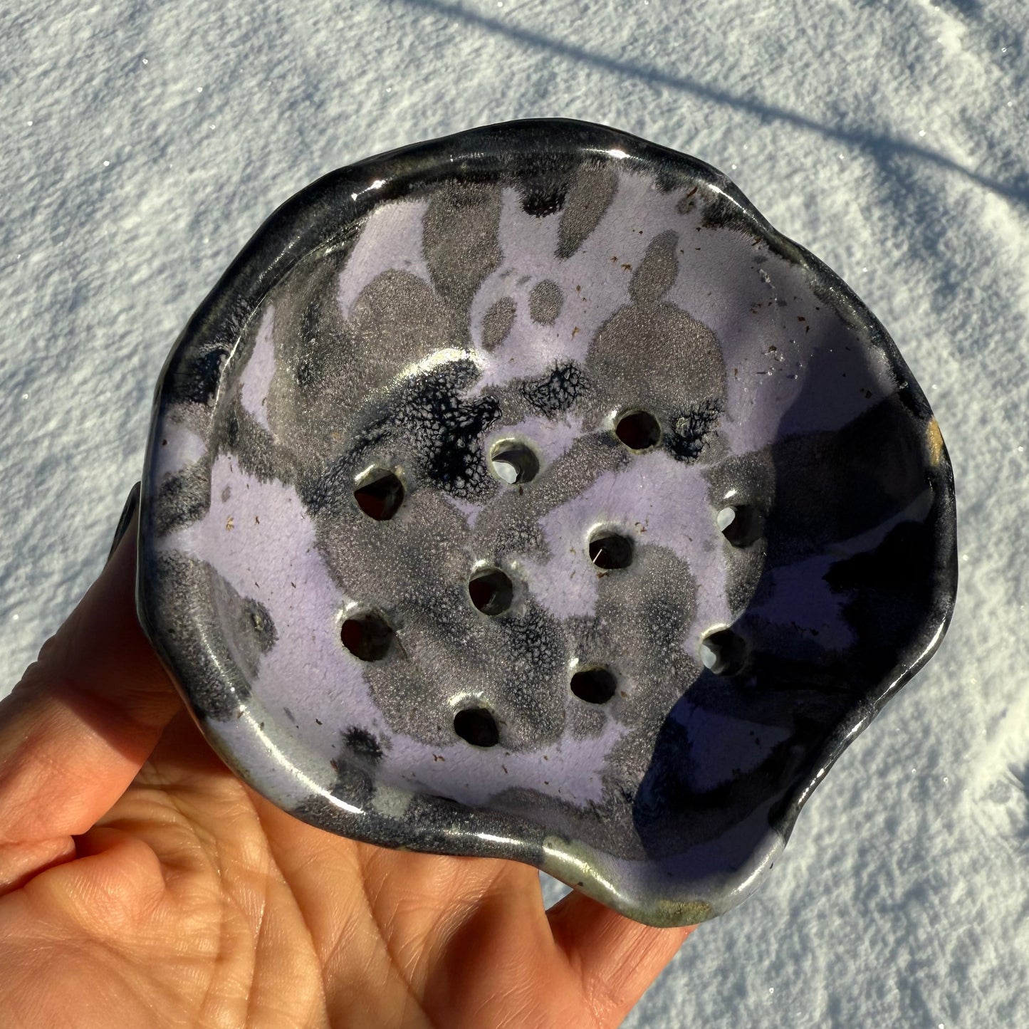 Hand holding a ceramic soap dish against a snowy background