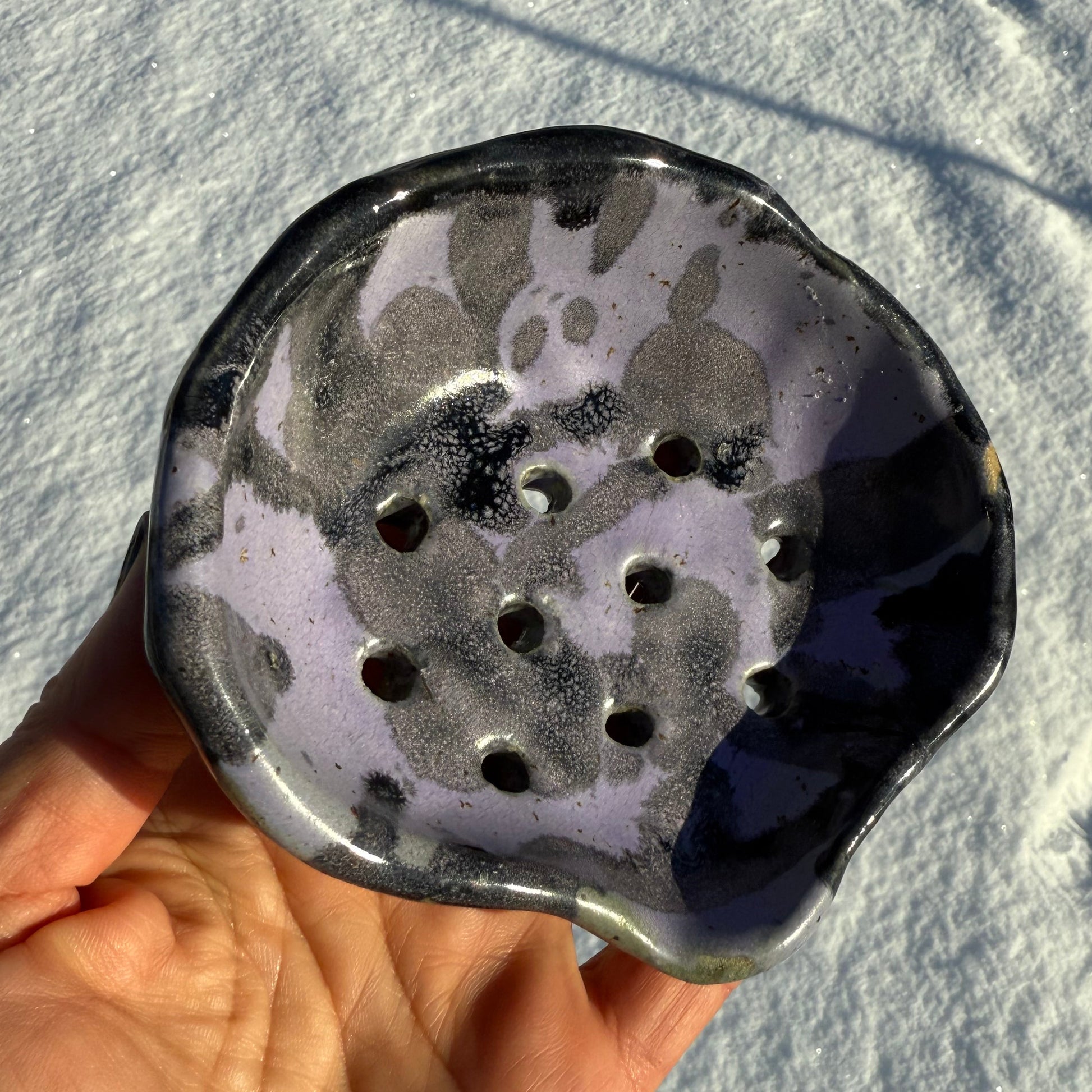 Hand holding a ceramic soap dish against a snowy background
