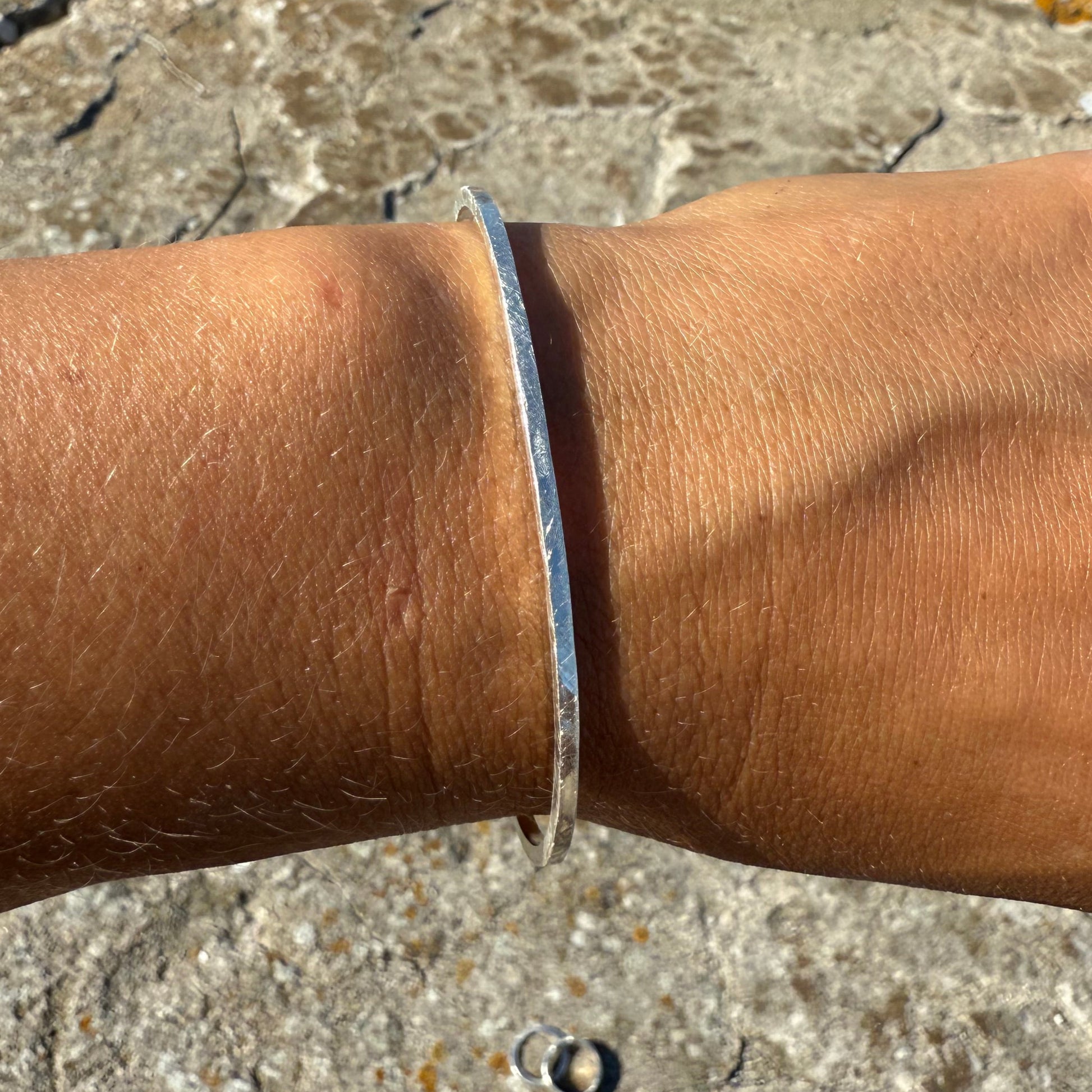 Close-up of a person's arm with a silver25 cuff bracelet with stone wall in the background