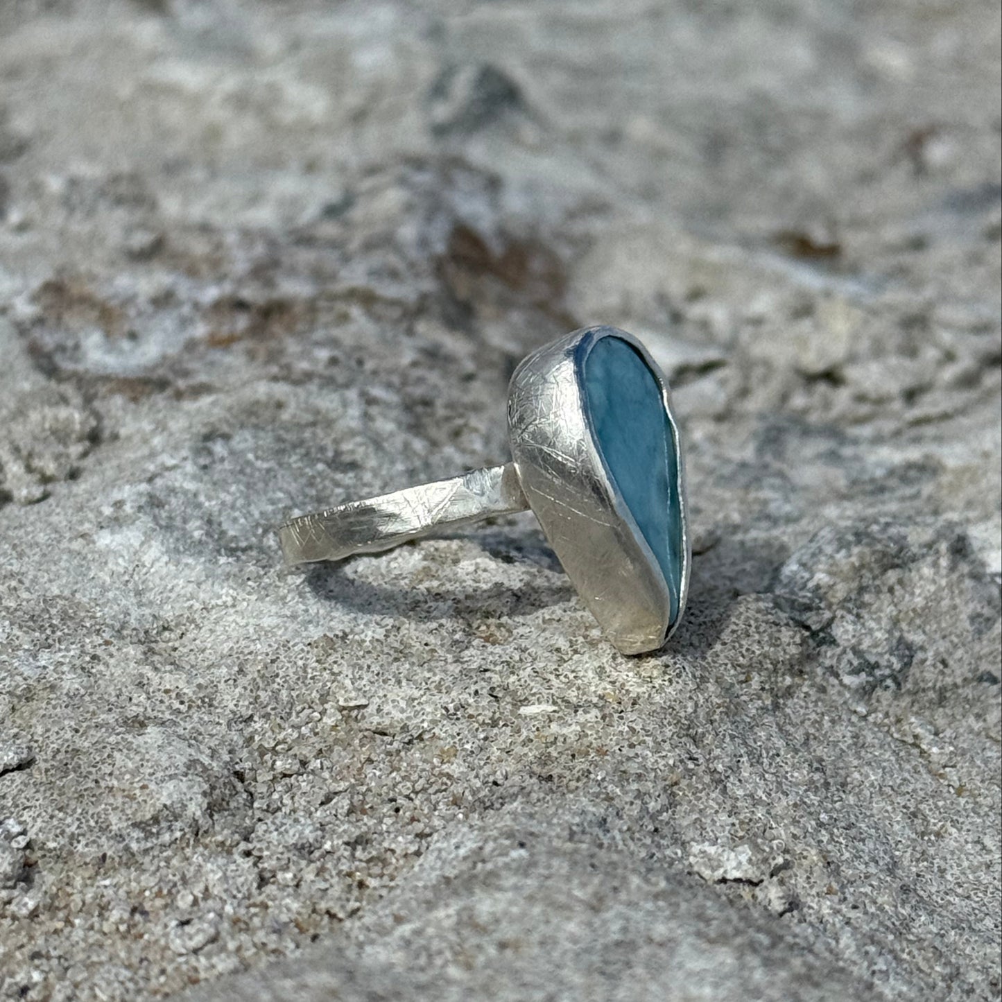 Silver ring with a blue and turquoise larimar stone on a textured stone surface