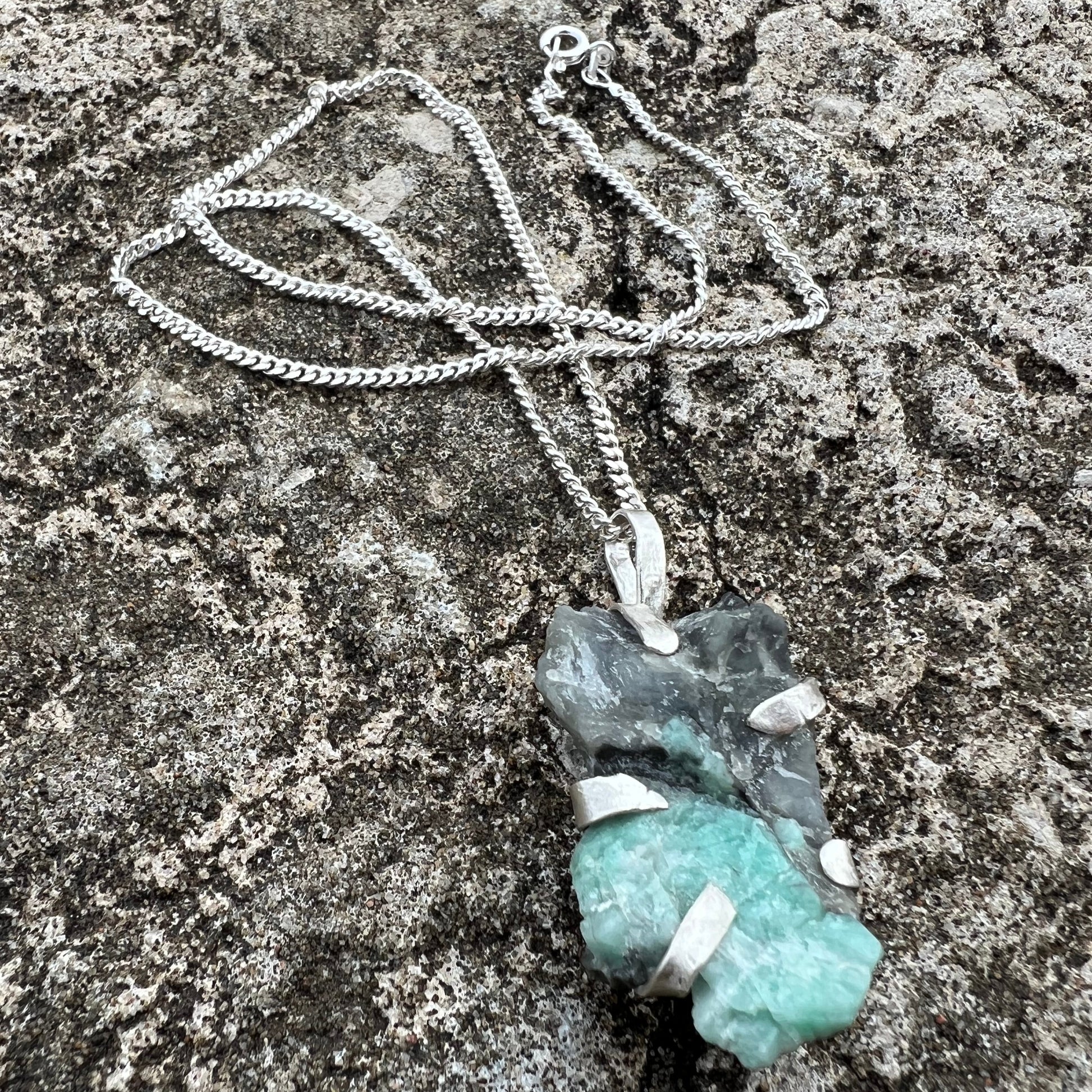 raw emerald crystal in green and black wrapped in sterlingsilver with silver chain on a textured surface